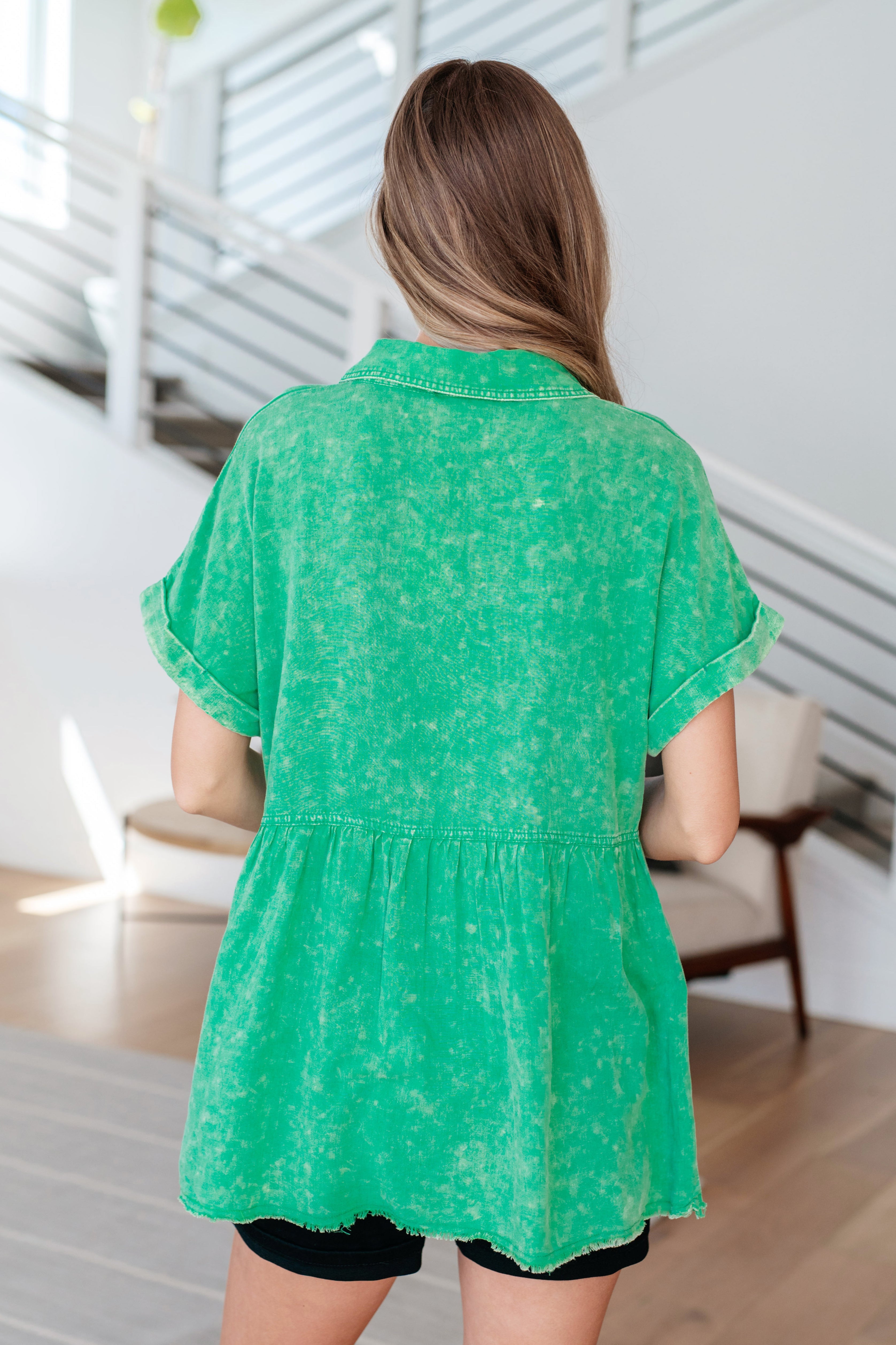 Woman with long brown hair wearing bright green button-up blouse with peplum hem and rolled short sleeves indoors