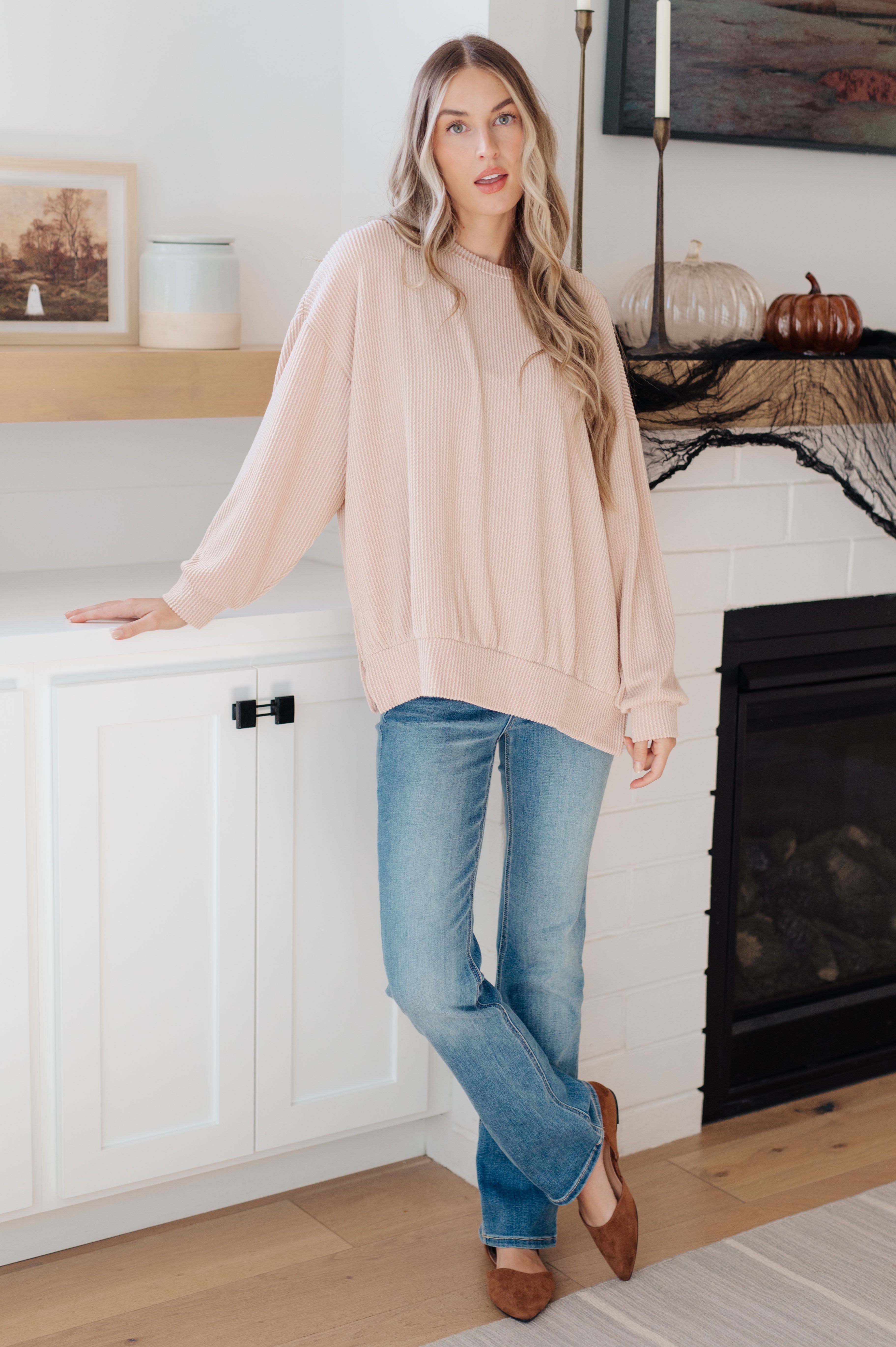 Woman wearing beige oversized pullover with ribbed texture paired with blue jeans and brown flats indoors