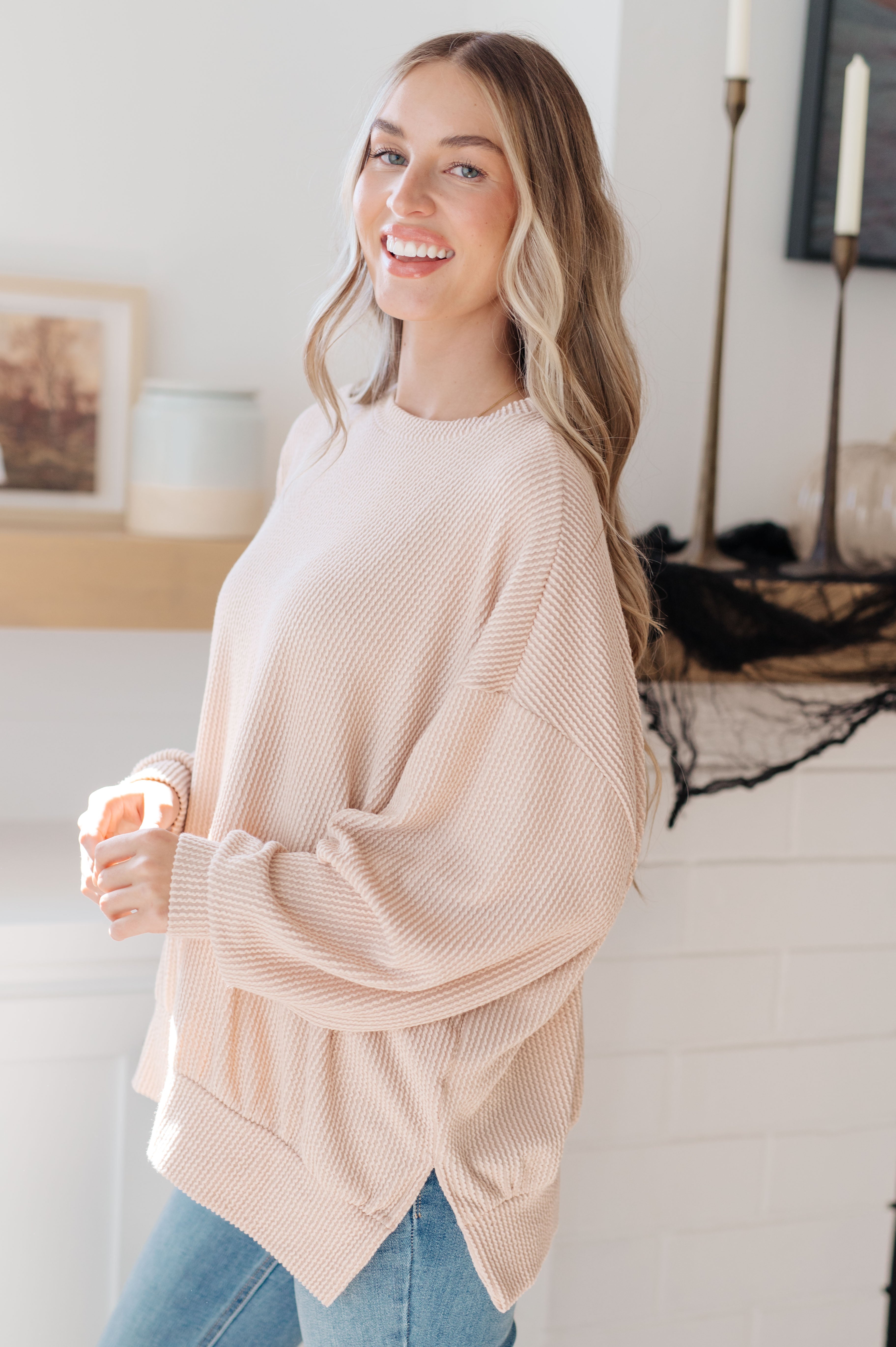 Smiling woman wearing a beige oversized pullover paired with light blue jeans in a bright cozy room