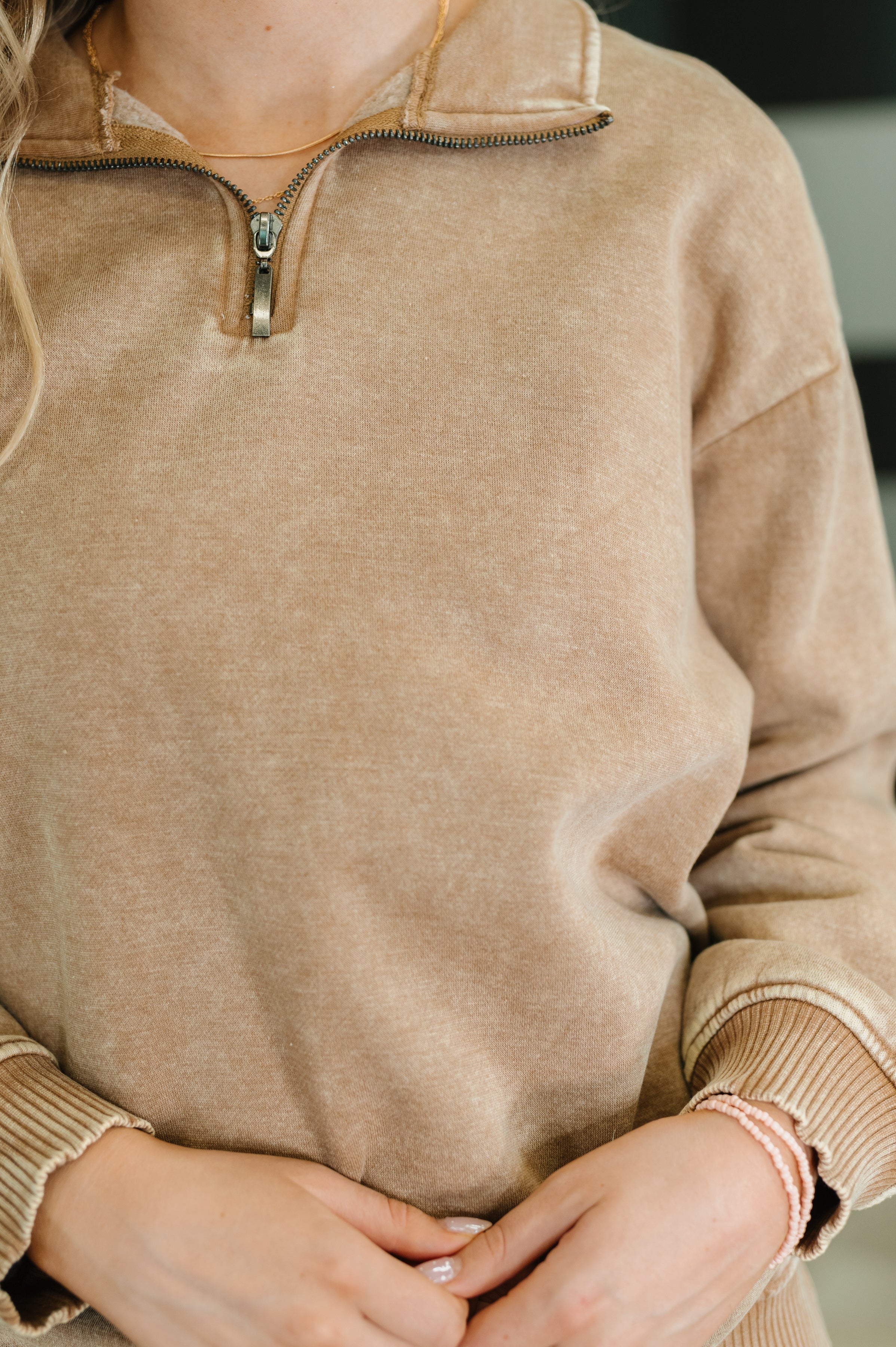 Close-up of camel half-zip pullover with ribbed cuffs worn with delicate gold necklace and light pink bracelet
