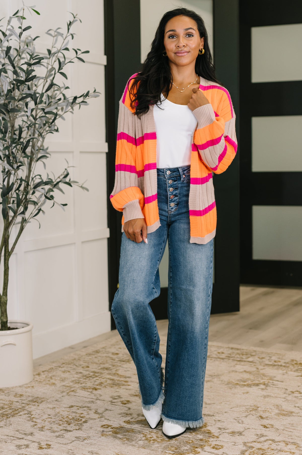 Woman wearing an orange striped open front cardigan over a white top with wide leg jeans in a modern home interior