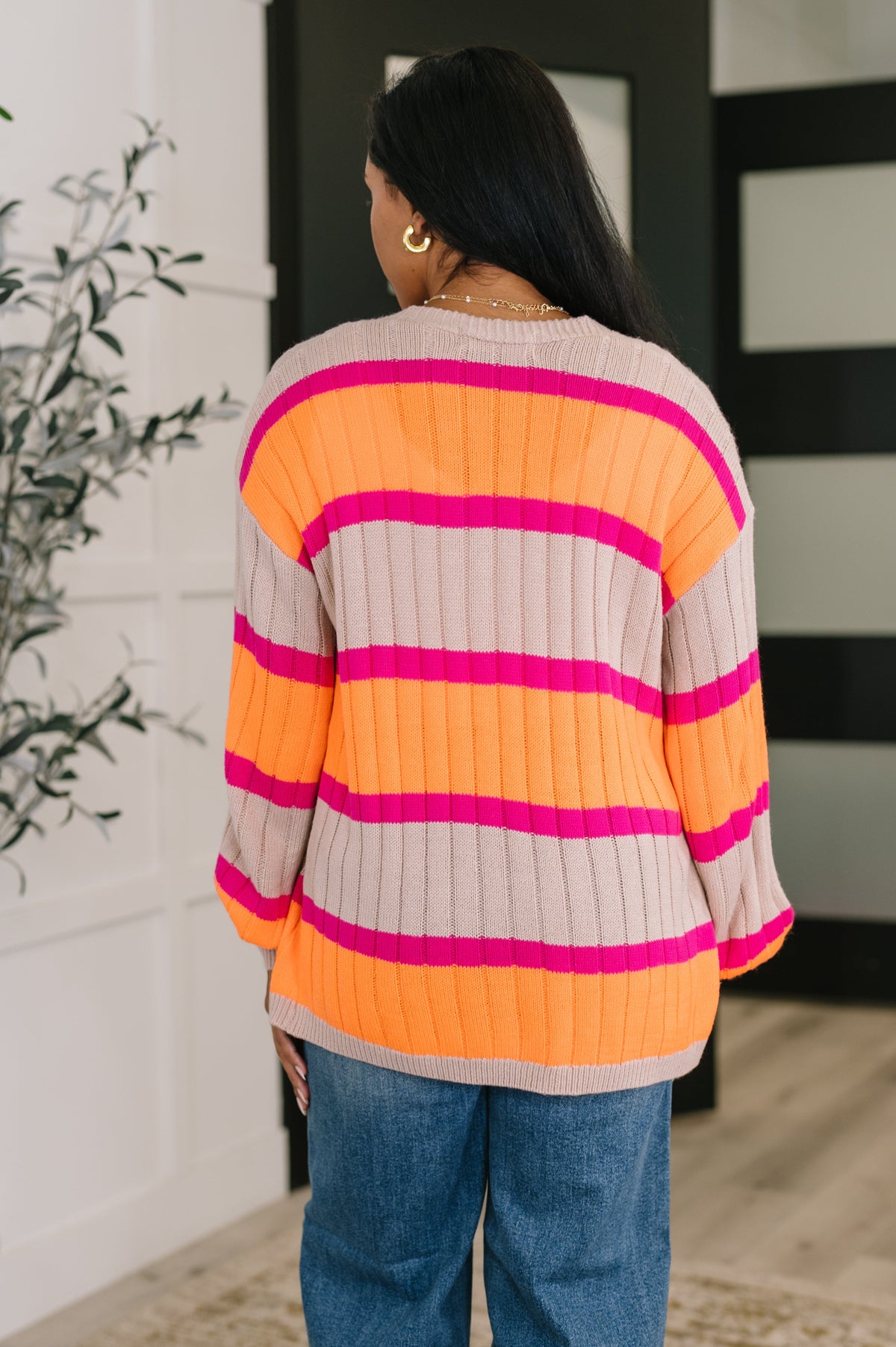 Back view of a woman wearing an orange striped cardigan with jeans in a bright modern home interior