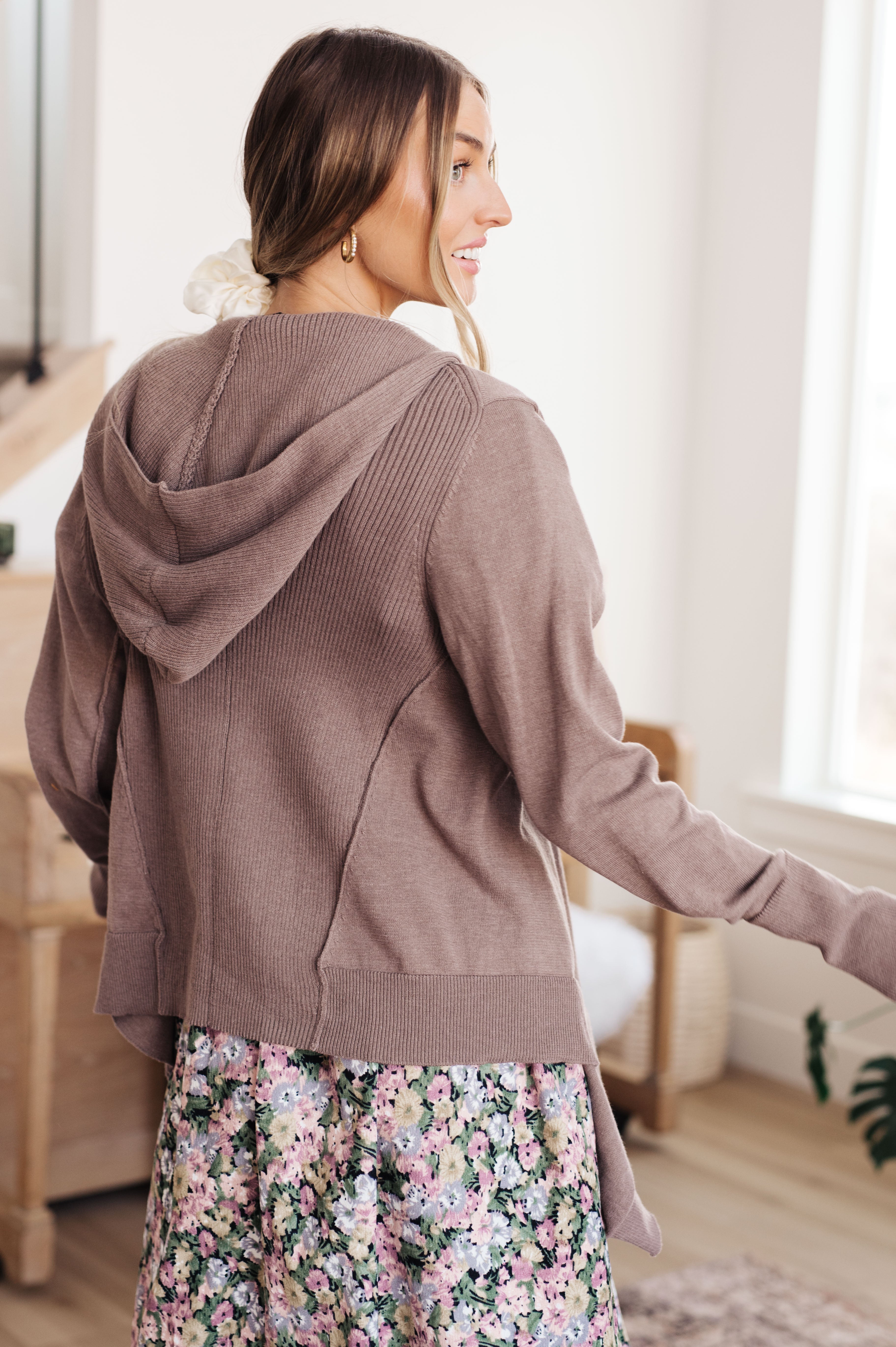 Woman wearing mocha knit cardigan with hood paired with floral skirt in bright indoor setting
