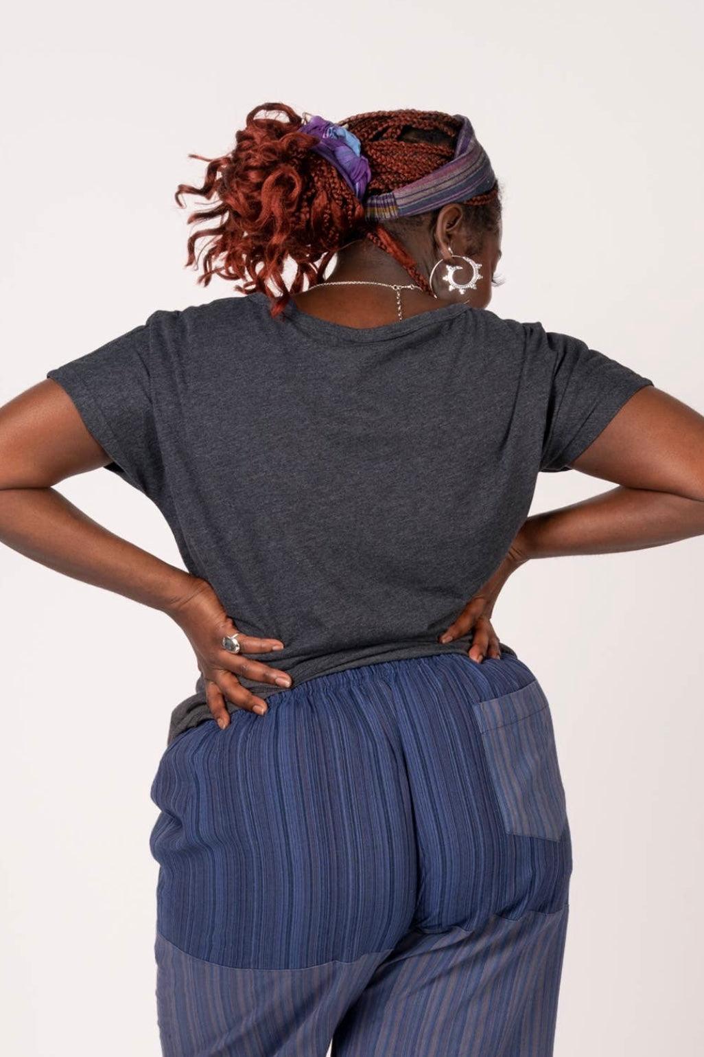 Woman with braided hair and purple headscarf wearing a charcoal slouchy top and loose striped pants facing away