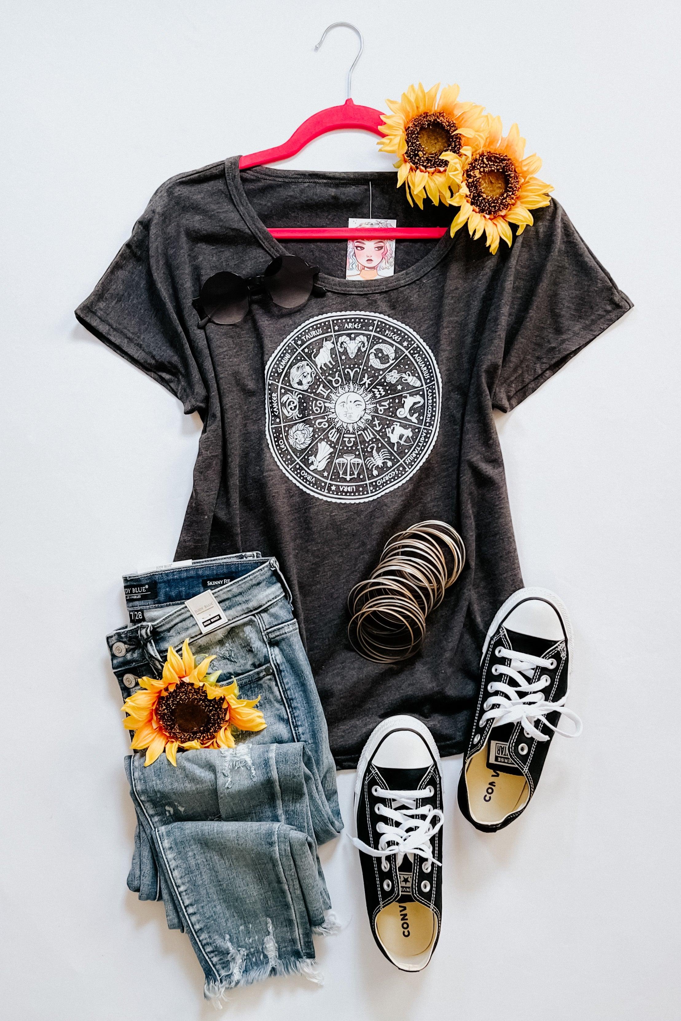 Charcoal zodiac-themed slouchy top paired with distressed jeans, black sneakers, sunglasses, bracelets, and sunflower accents