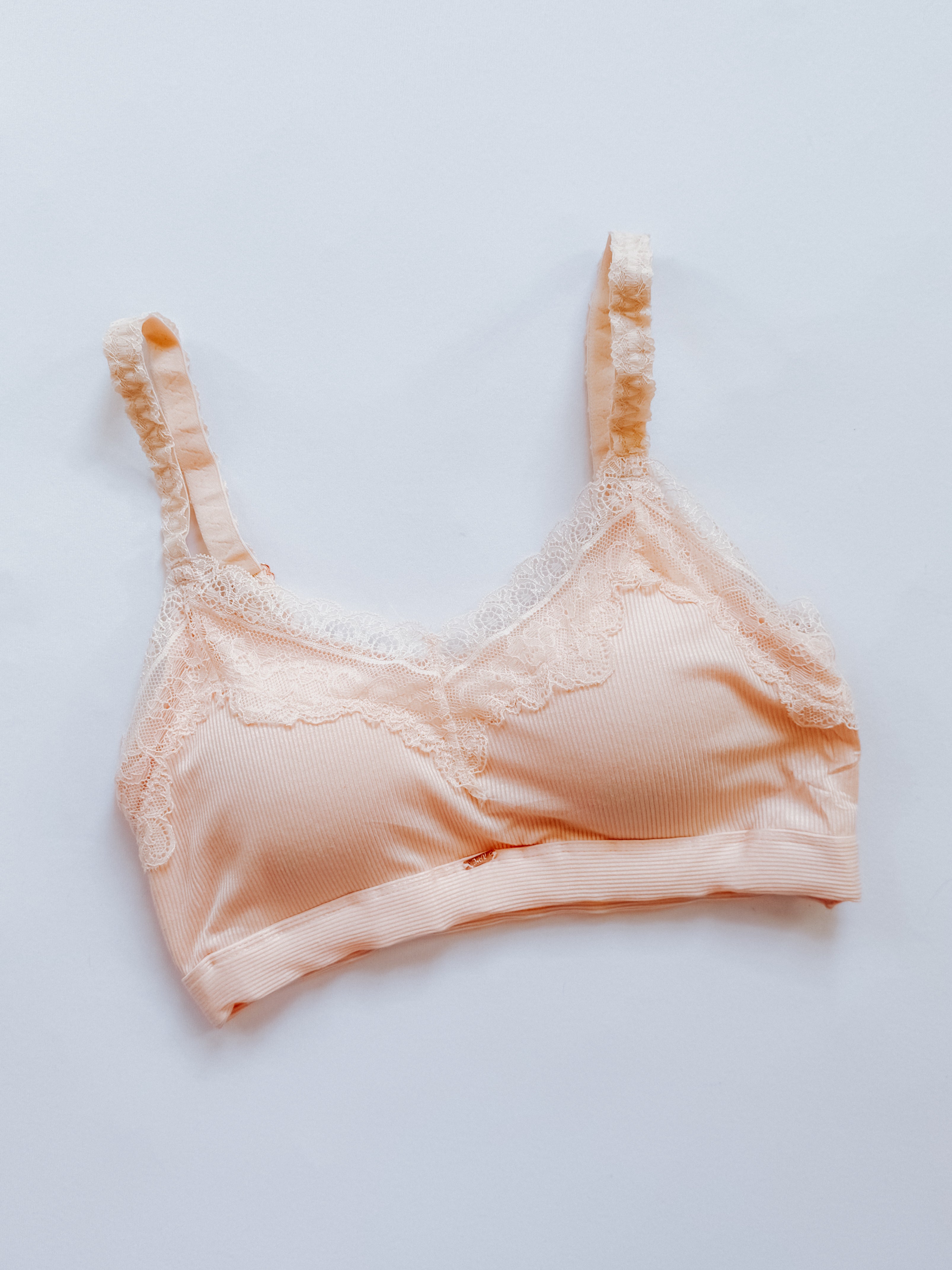 Peach lace-trim bralette with adjustable straps and delicate detailing laid flat on white background