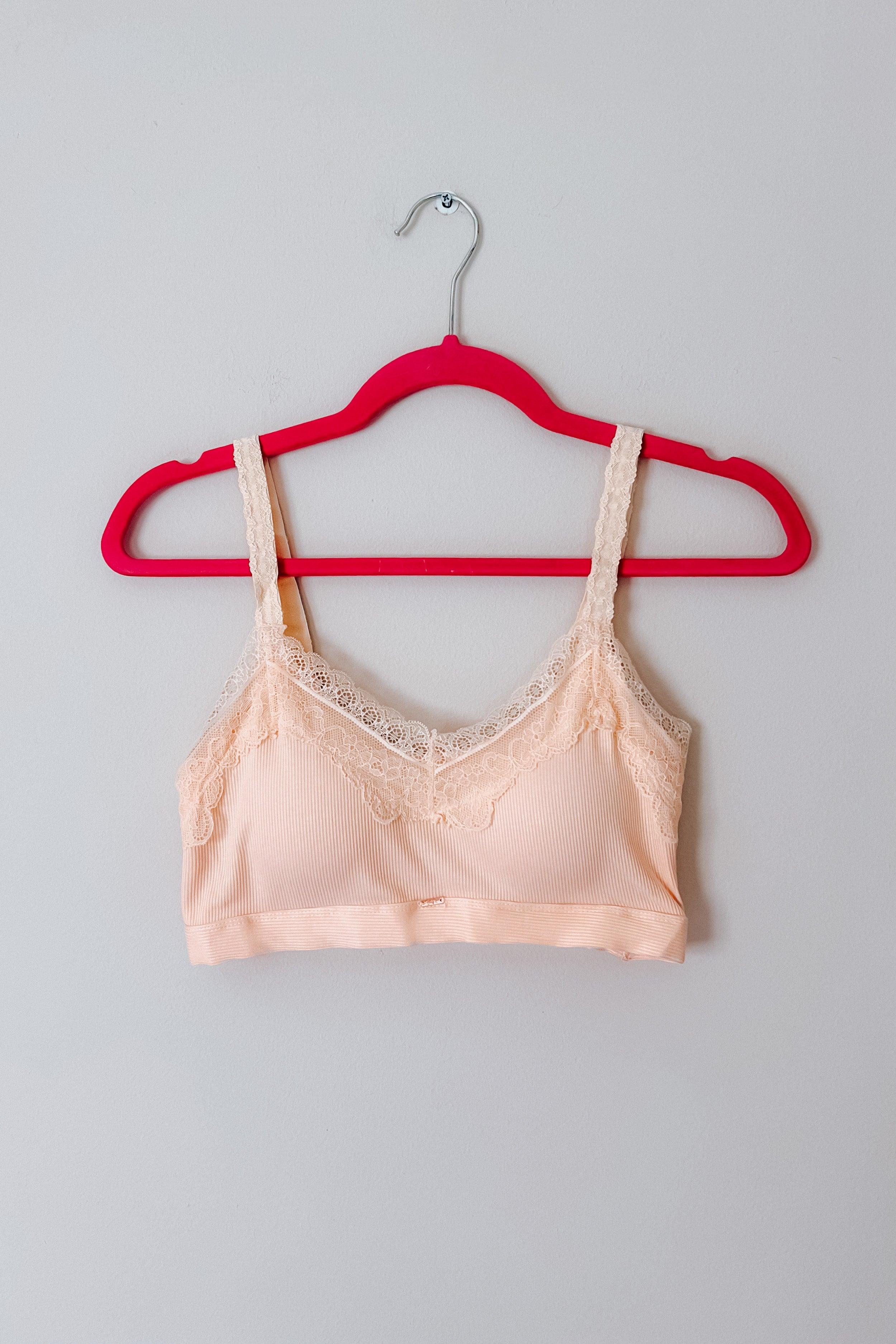 Peach lace-trim bralette with delicate straps displayed on a vibrant red hanger against plain background