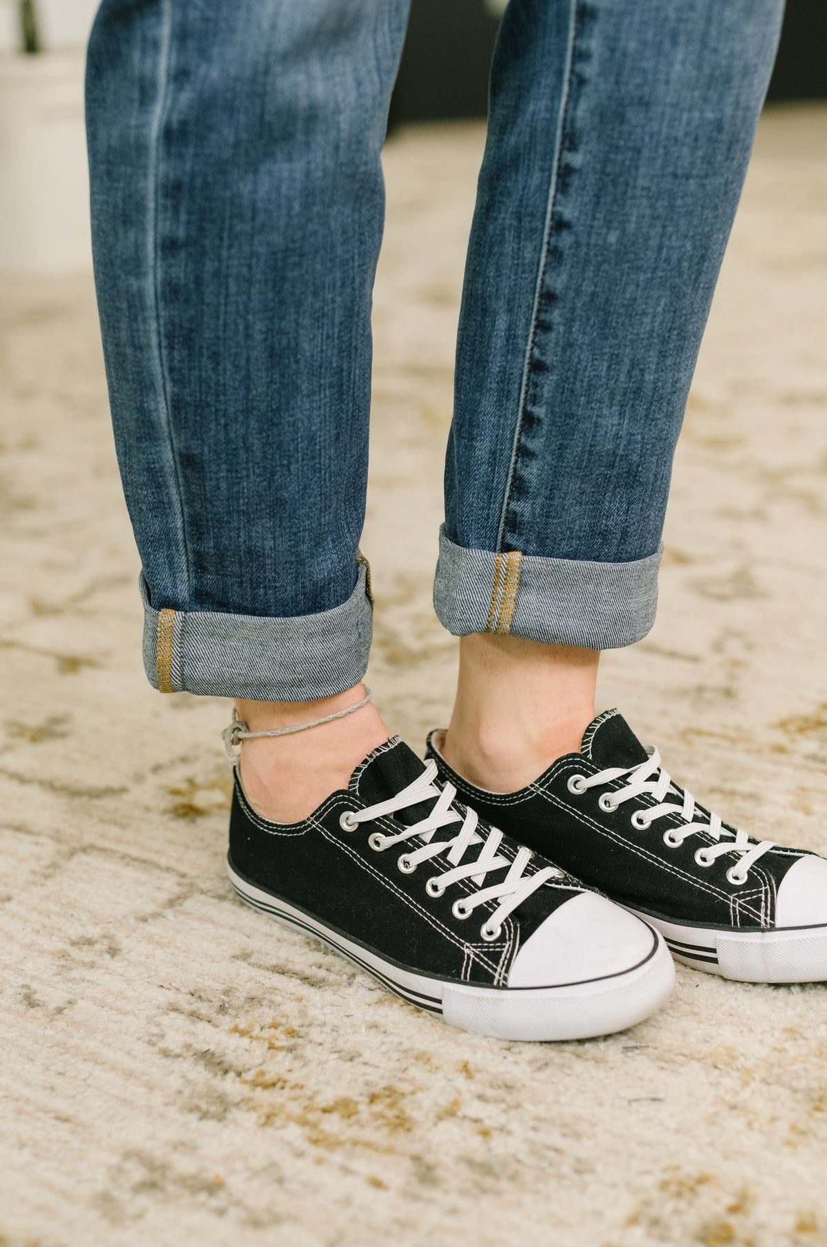 Close-up of blue boyfriend jeans with rolled cuffs styled with black canvas sneakers and white rubber toes indoors