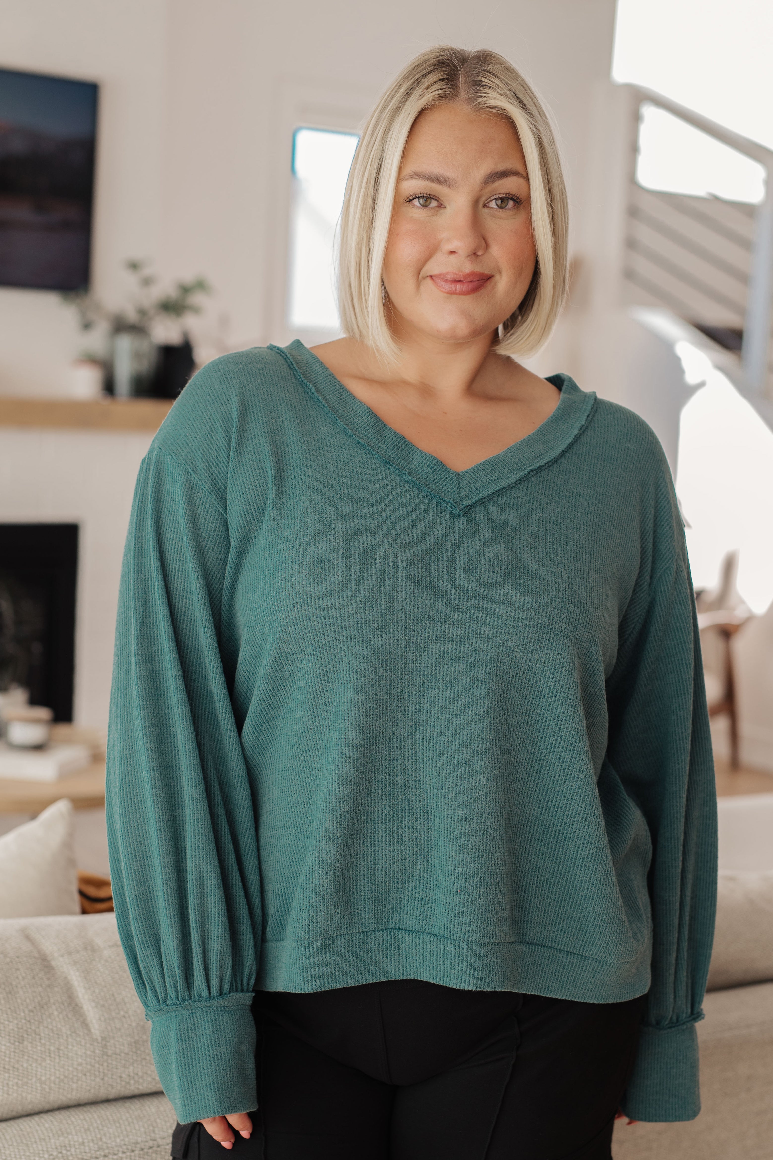 Woman wearing a teal sweater and black pants in an indoor setting