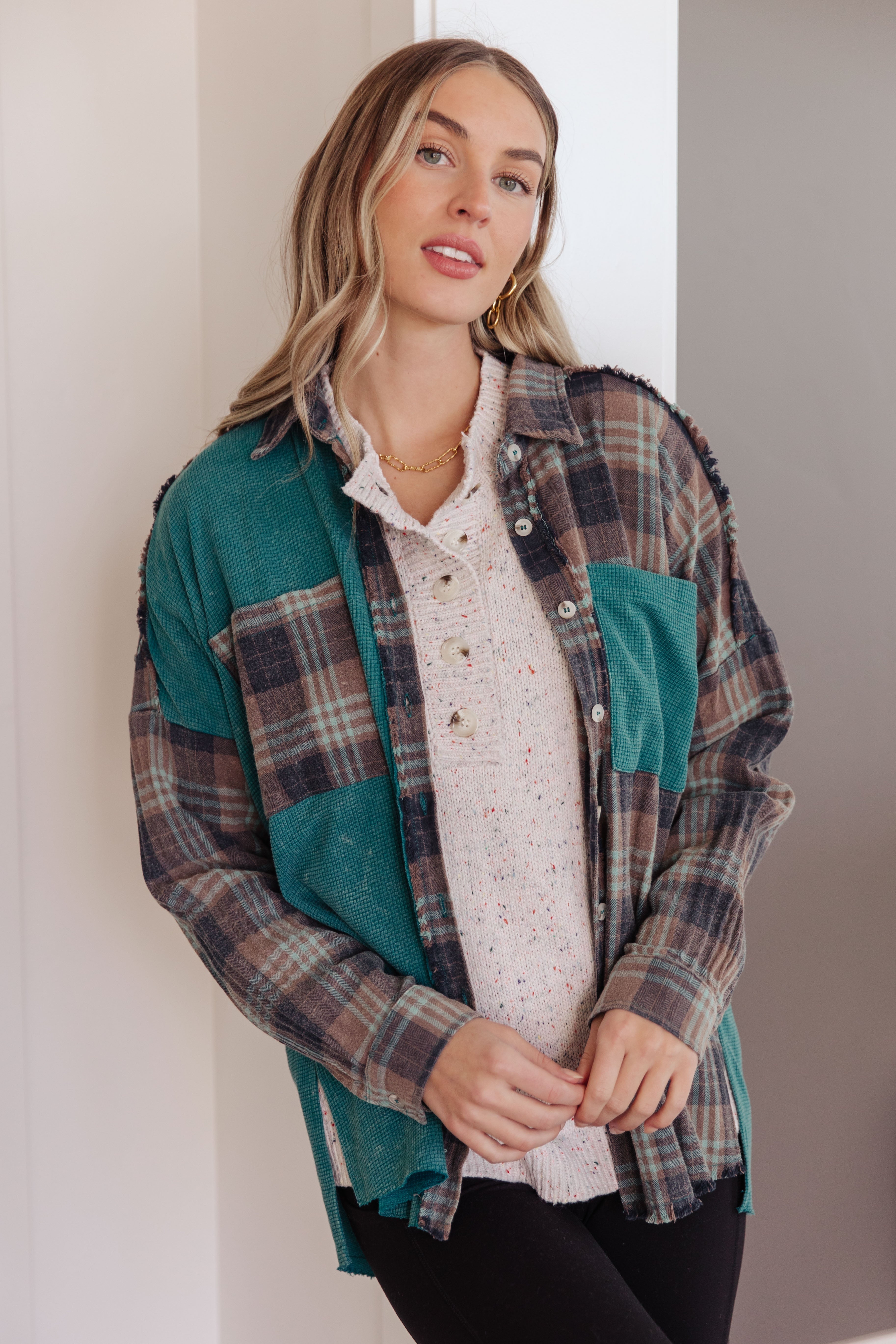 Woman wearing a blue plaid button up shirt over a beige sweater with black leggings in an indoor setting.