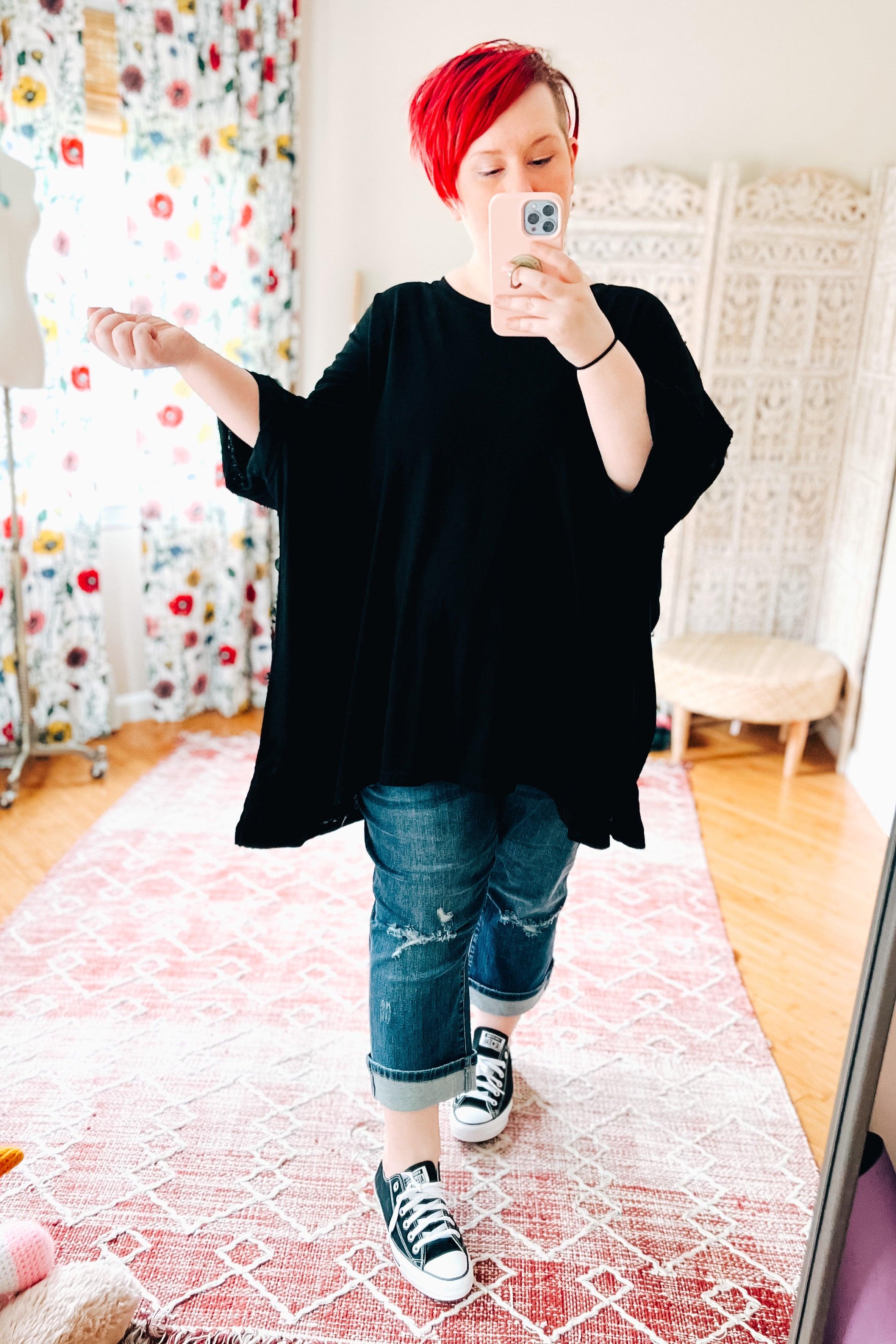 Woman with short red hair wearing oversized black All My Life Boxy Top and rolled distressed jeans taking selfie indoors