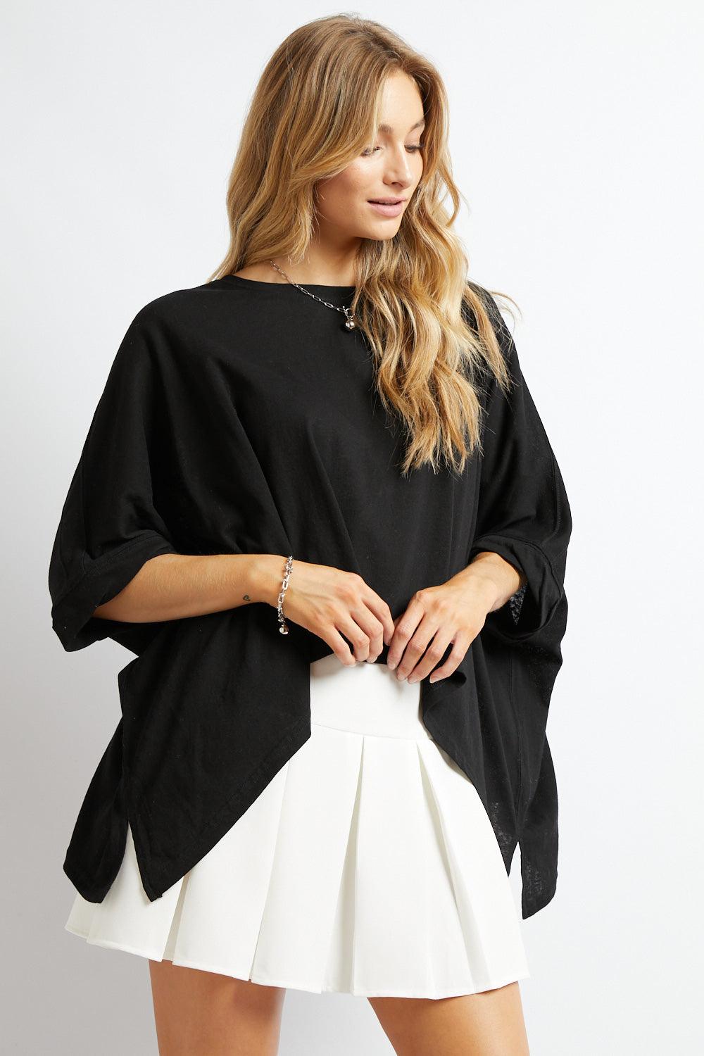 Woman wearing black All My Life Boxy Top with rolled sleeves paired with white pleated mini skirt against white background