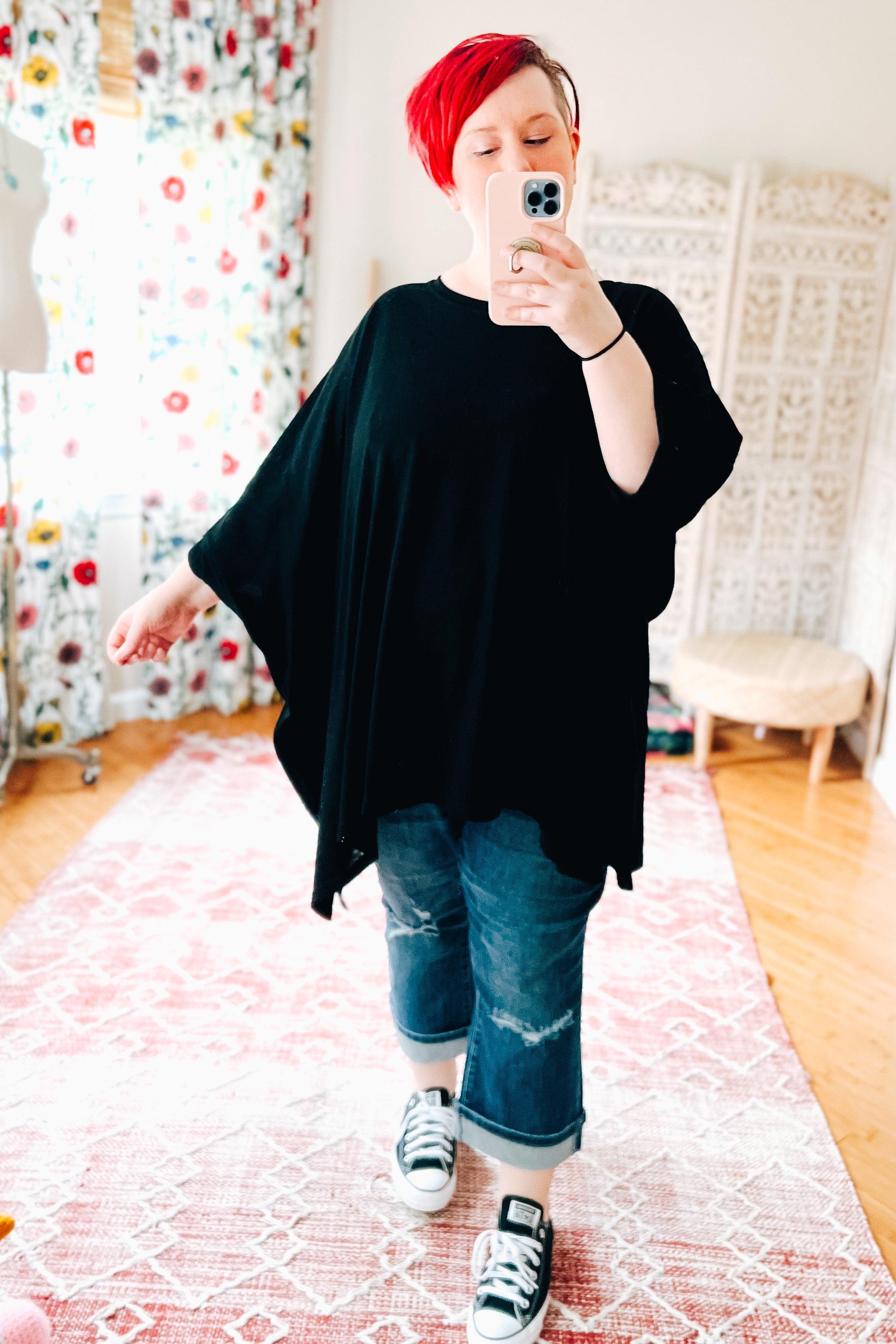 Woman with short red hair wearing oversized black All My Life Boxy Top and rolled jeans taking selfie indoors