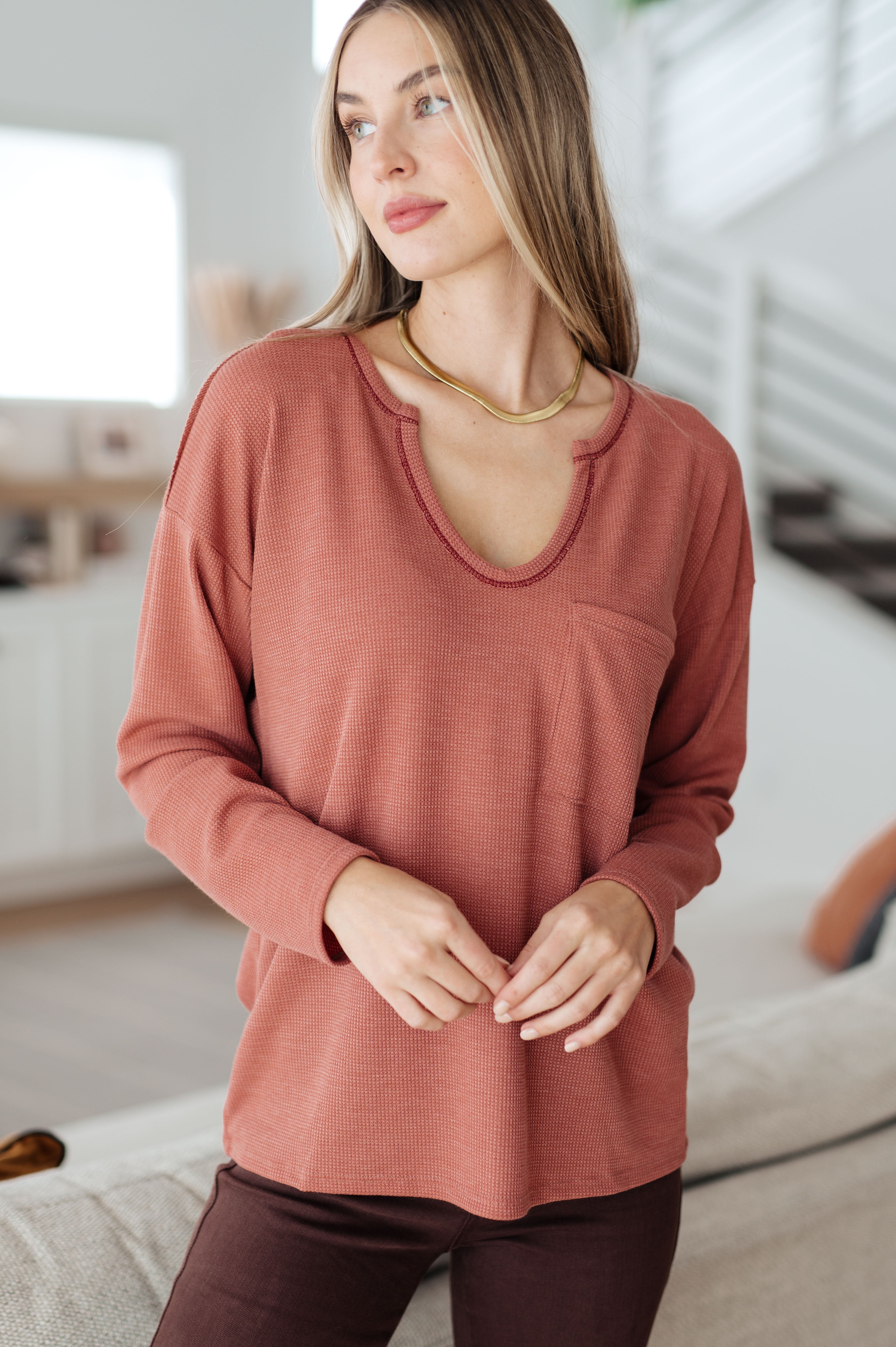 Woman wearing rust-colored Behind The Scenes waffle knit top with raw edge neckline and chest pocket indoors
