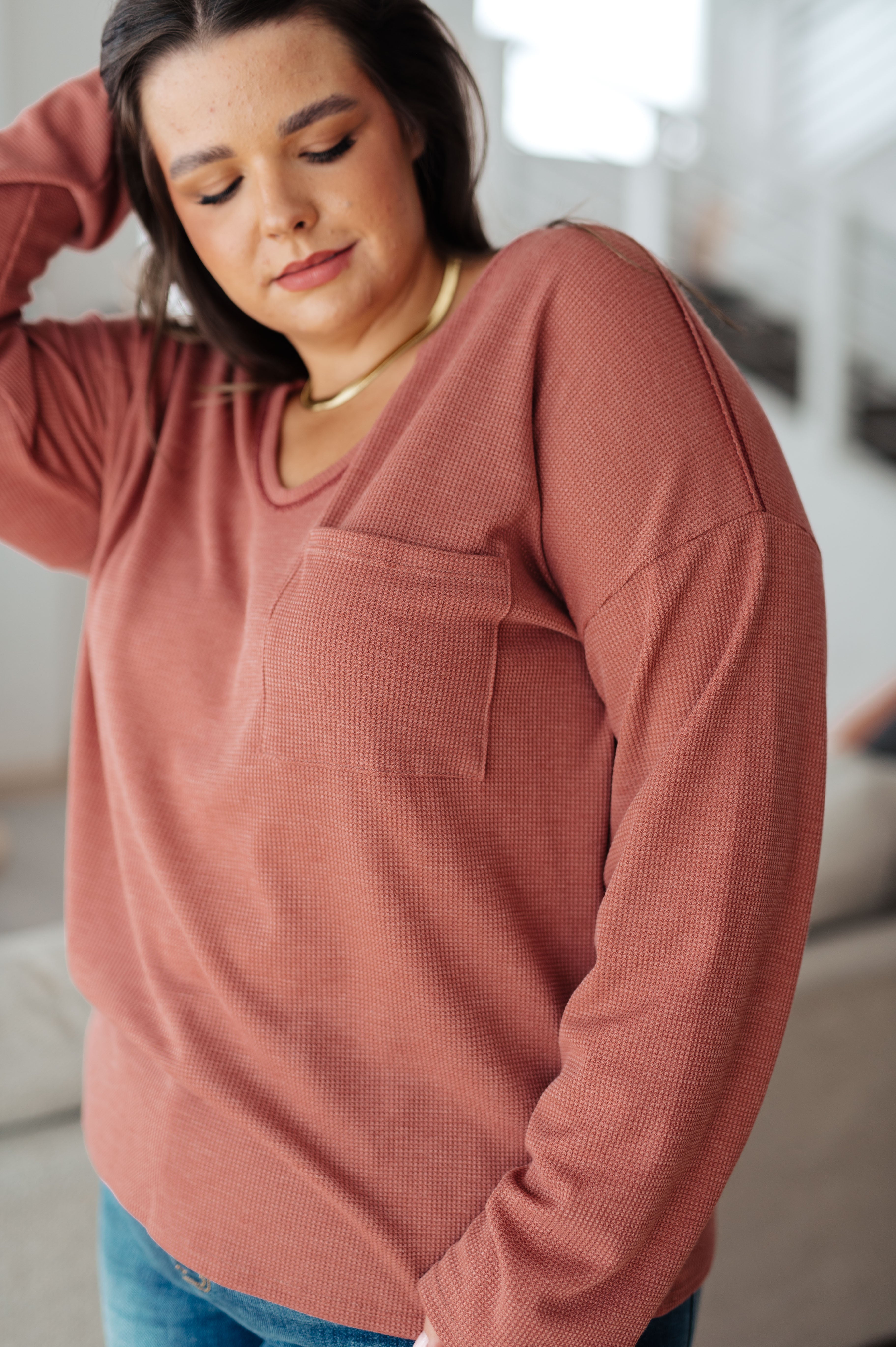 Close-up of woman wearing rust-colored Behind The Scenes waffle knit top with chest pocket in casual indoor setting