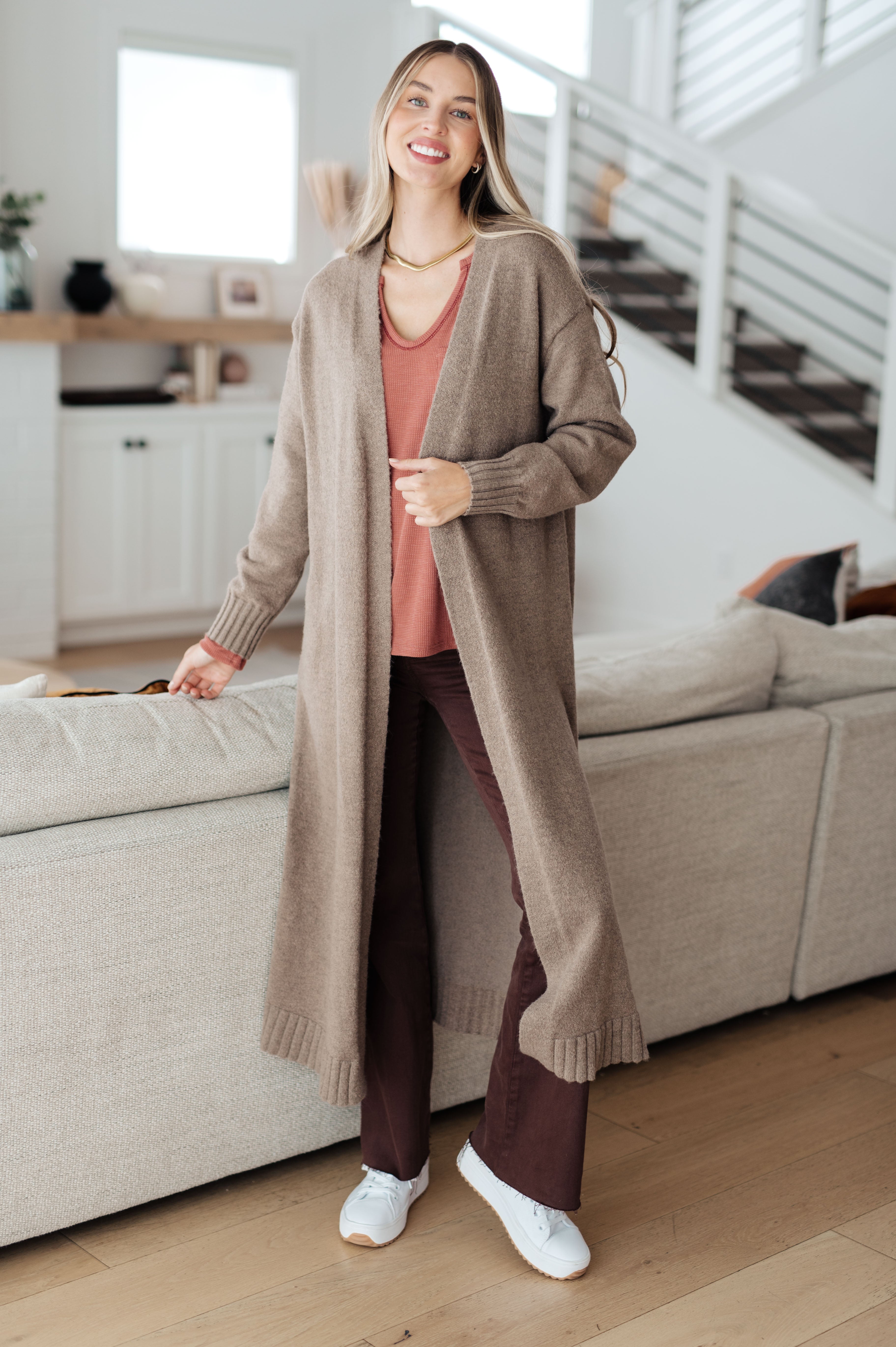Smiling woman in rust-colored Behind The Scenes waffle knit top wearing long beige cardigan and white sneakers indoors