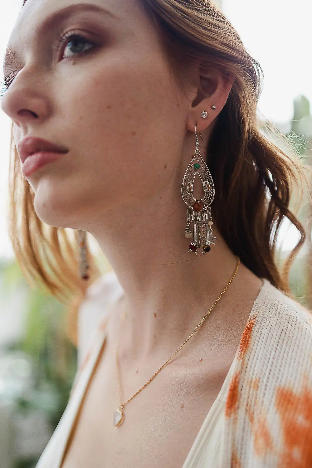 Close-up of woman wearing large silver teardrop earrings with dangling charms and beads, also wearing a delicate crescent moon necklace