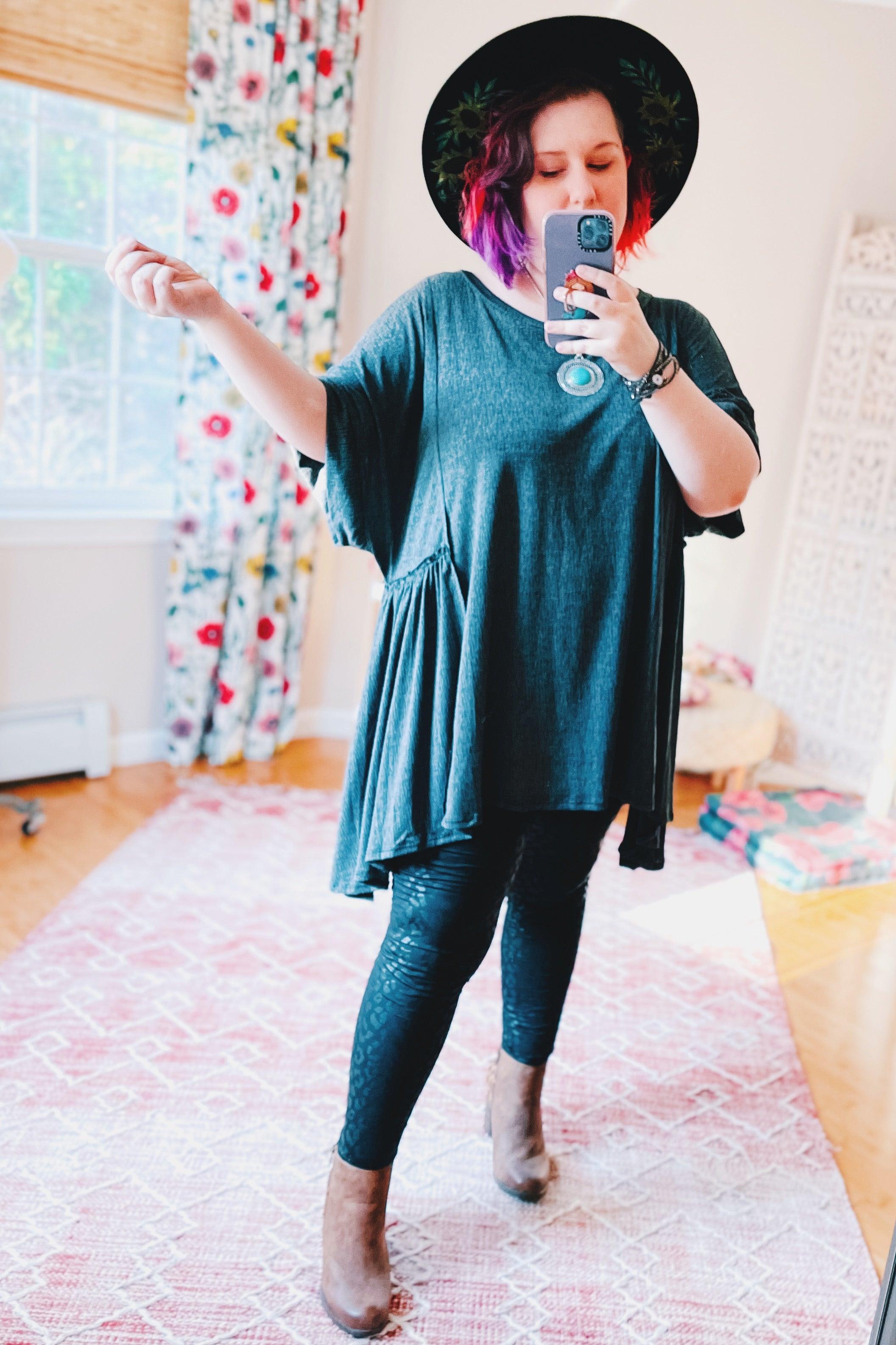 Woman wearing oversized dark gray tunic with short sleeves, paired with black leggings and brown ankle boots indoors