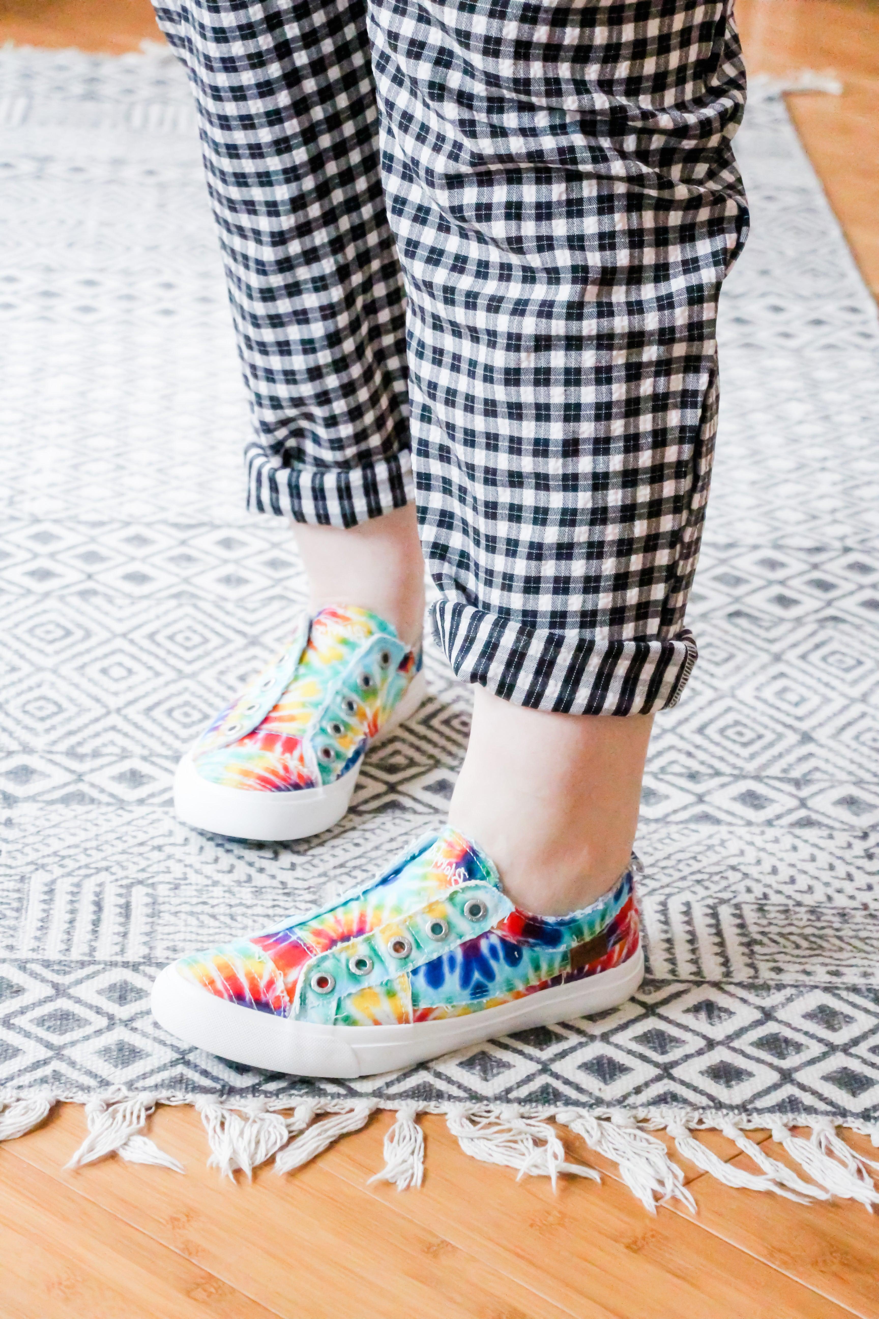 Low-top rainbow tie-dye canvas sneakers with white rubber sole worn with rolled black and white checkered pants