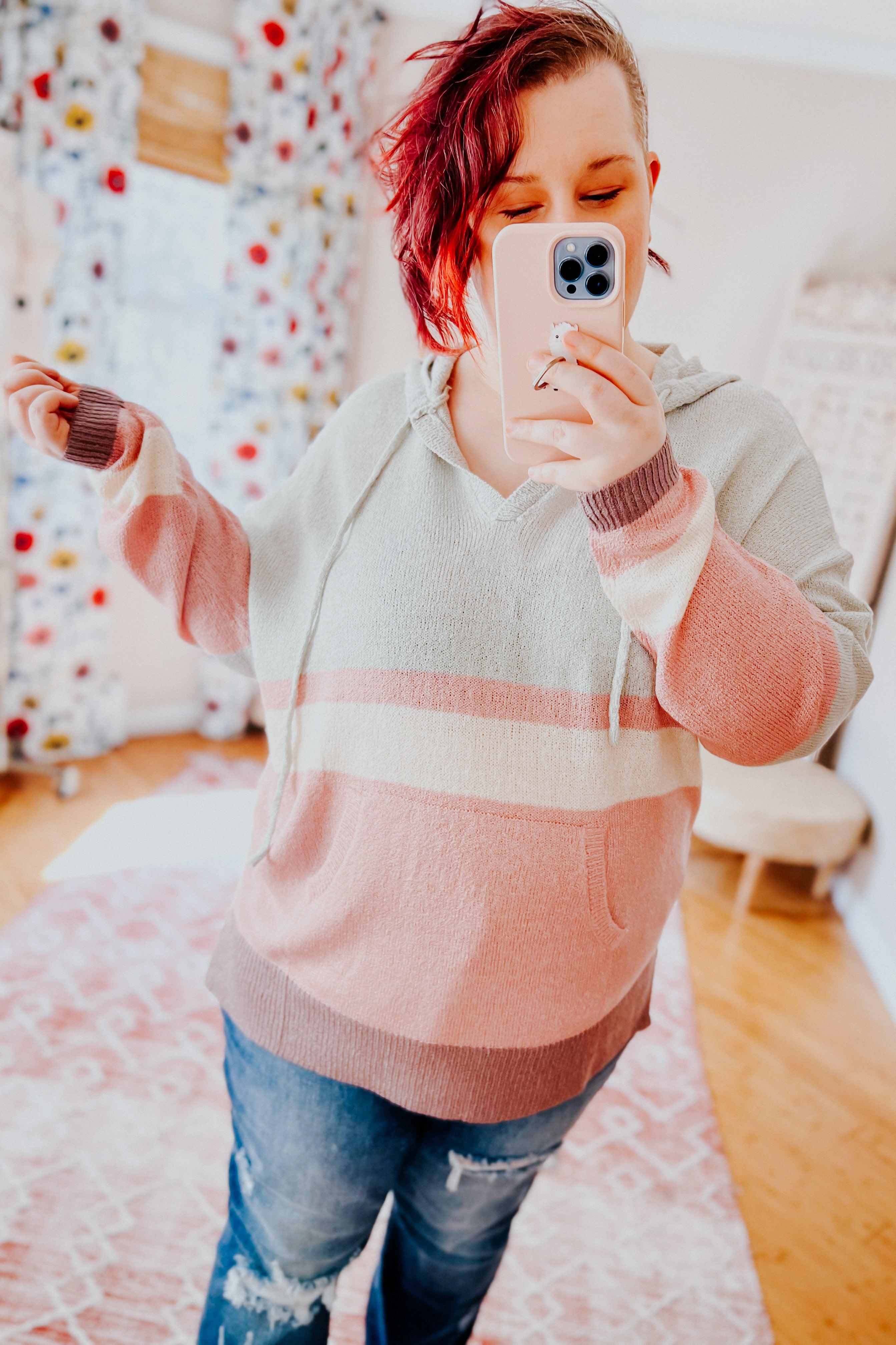 Woman with red hair wearing pastel striped Boy Spring Hoodie taking a mirror selfie indoors with ripped jeans