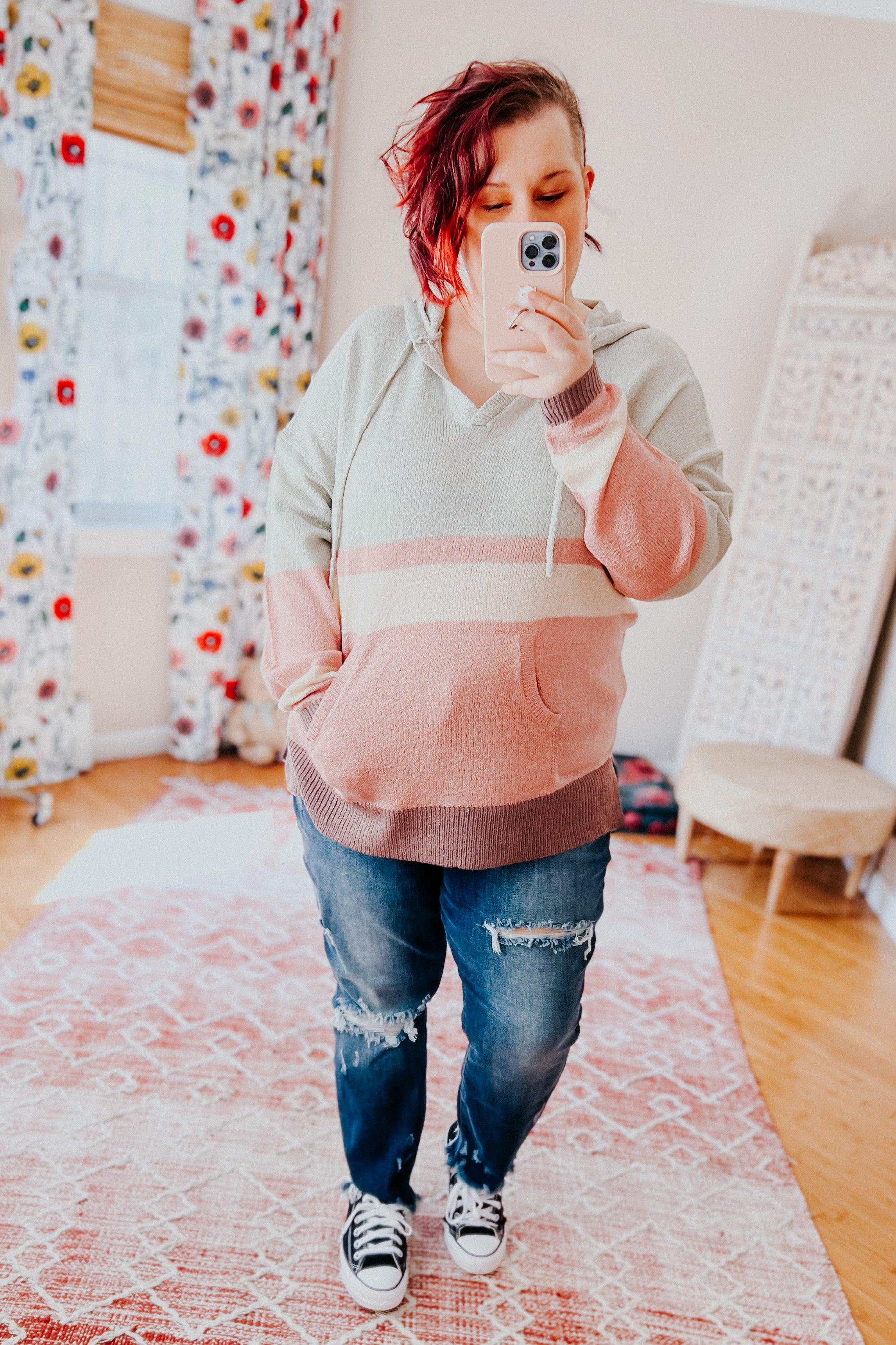 Woman with short red hair wearing pastel striped Boy Problem Spring Hoodie and ripped jeans taking a selfie indoors