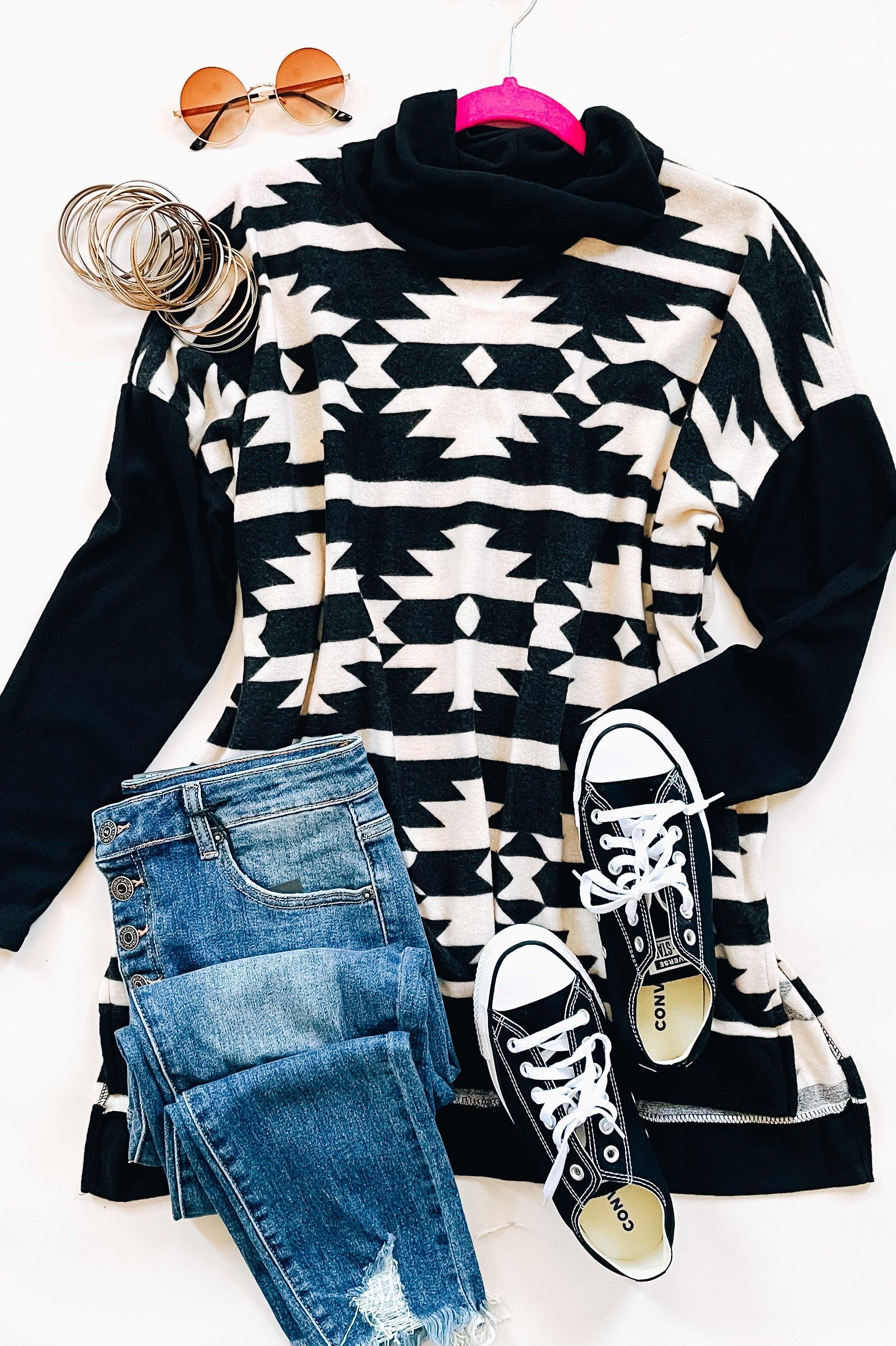 Black and white geometric patterned cowl neck pullover styled with distressed blue jeans, black sneakers, and round sunglasses