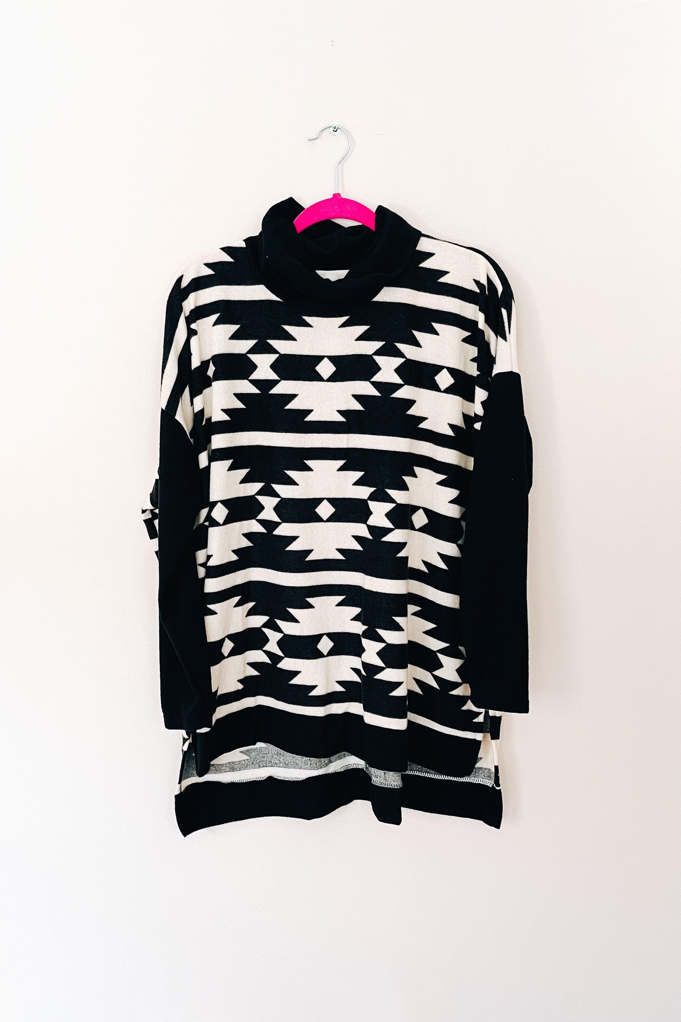 Black and white tribal print cowl neck pullover hanging on pink hanger against white wall