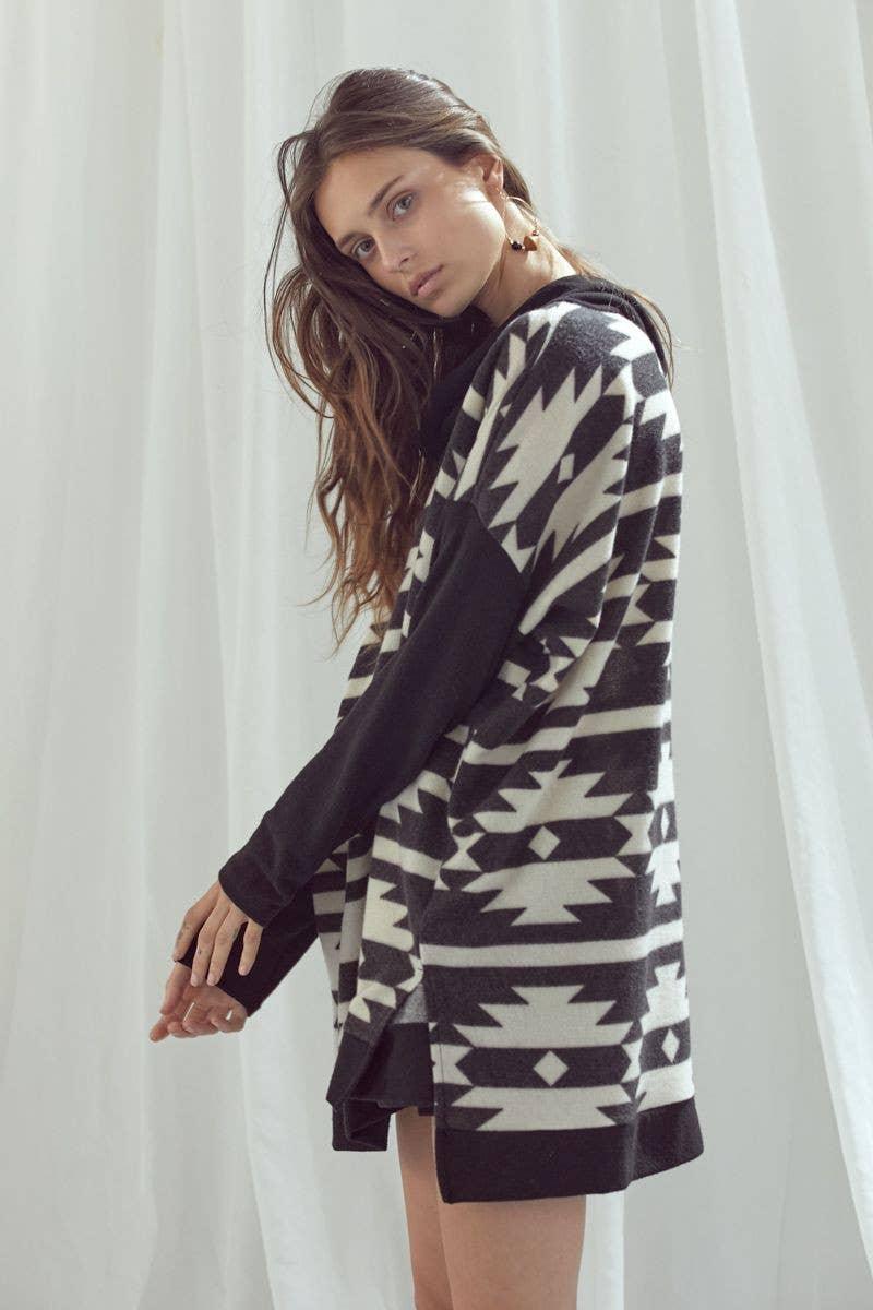 Woman wearing black and white geometric patterned cowl neck pullover with long sleeves standing sideways