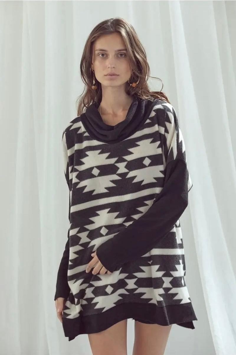Woman wearing oversized black and white geometric patterned cowl neck pullover with long sleeves indoors