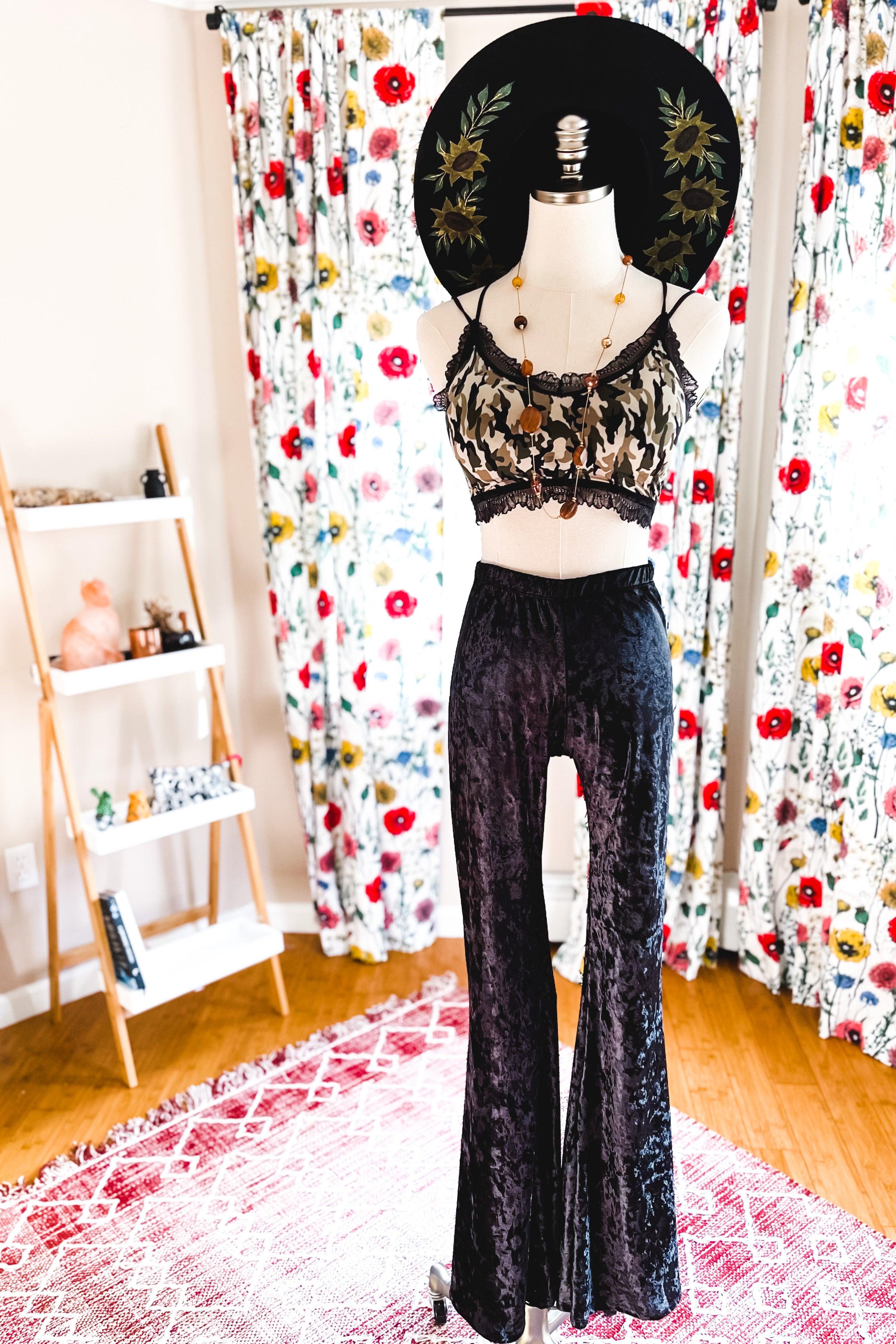 Mannequin dressed in camo bralette with black lace trim and black crushed velvet bell-bottom pants in bright room