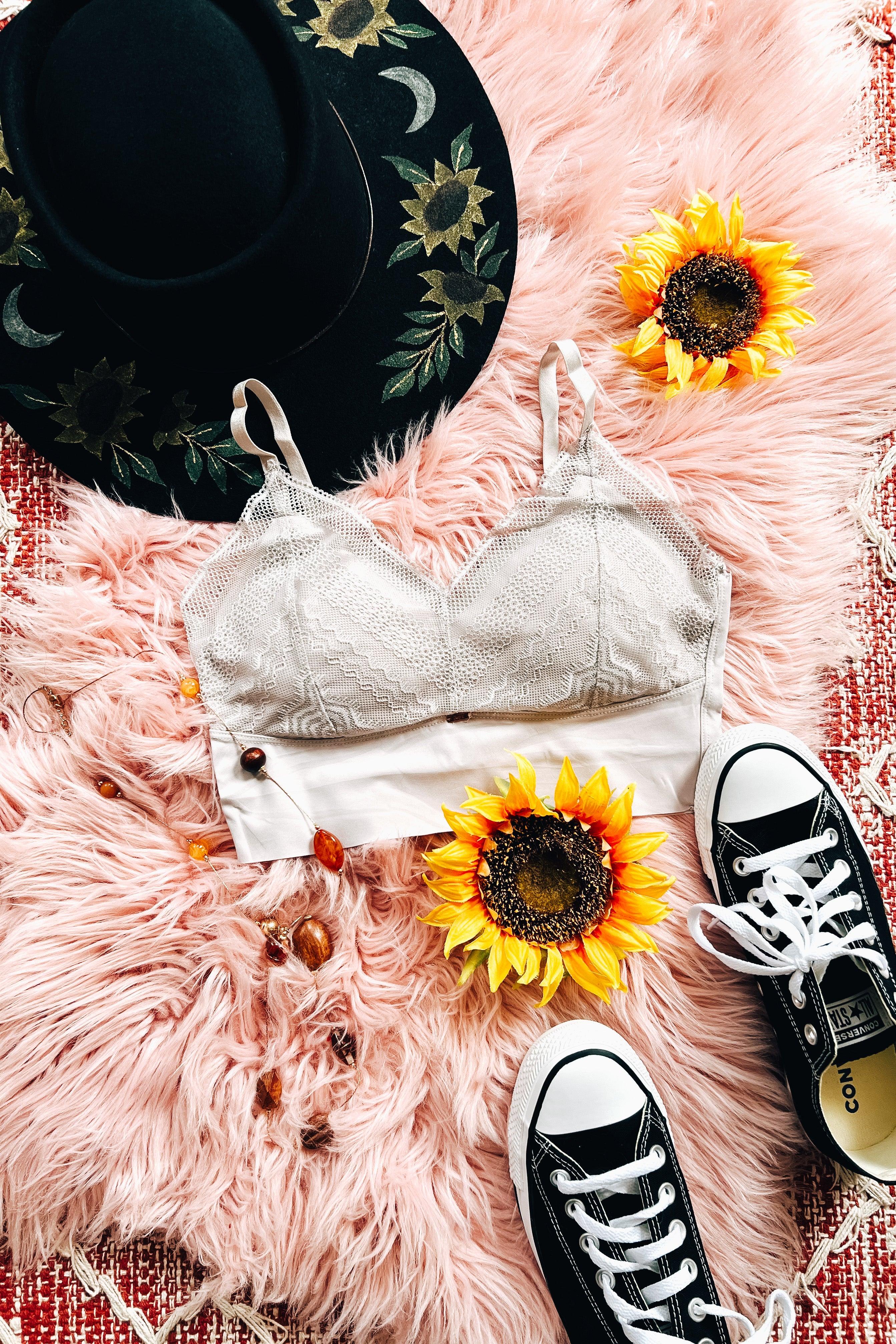 Silver lace bralette styled on pink faux fur with black embroidered hat, sunflowers, and black low-top sneakers