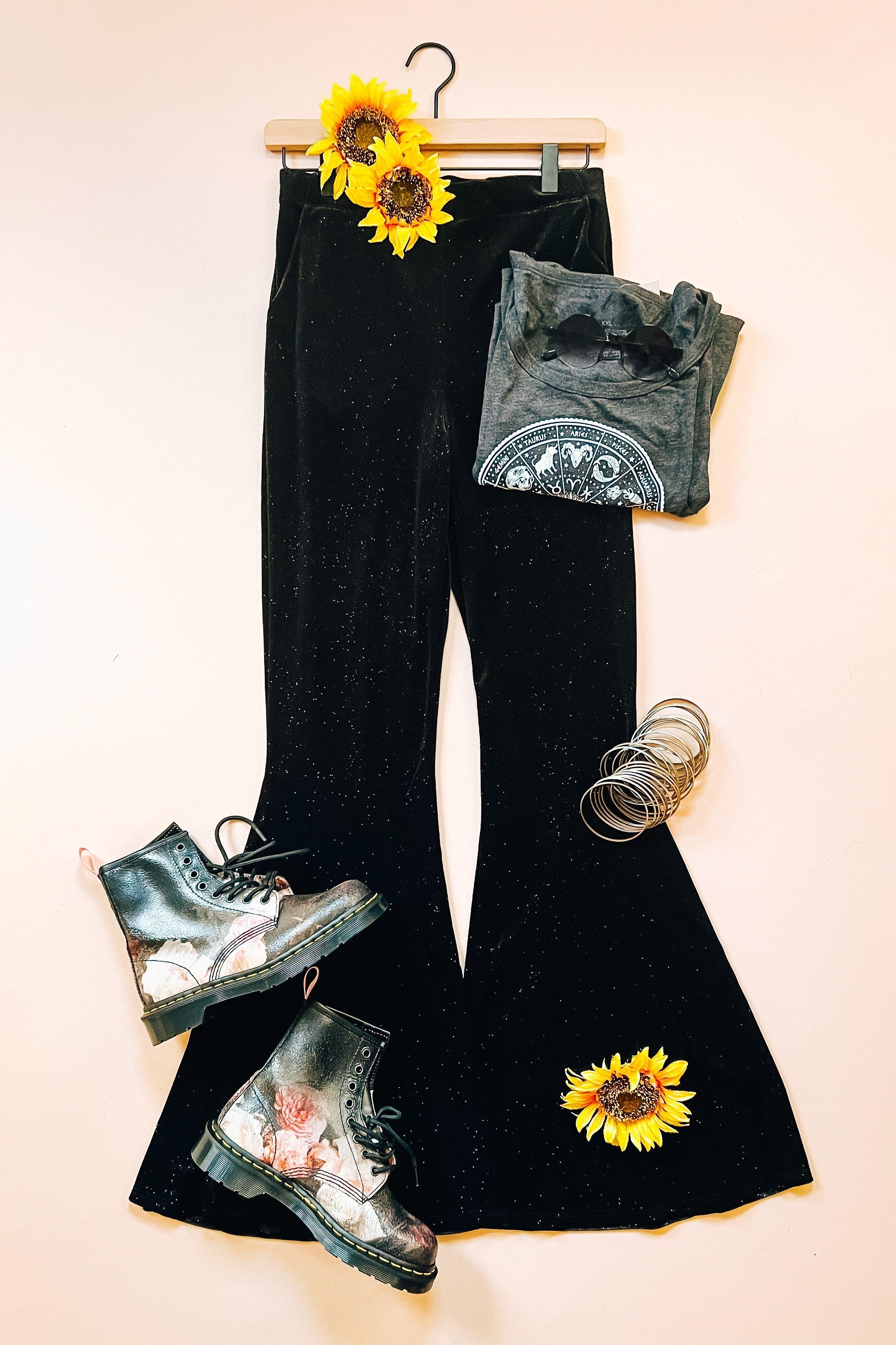 Black glitter bell bottoms styled with floral combat boots, folded graphic tee, silver bangles, and sunflowers on hanger