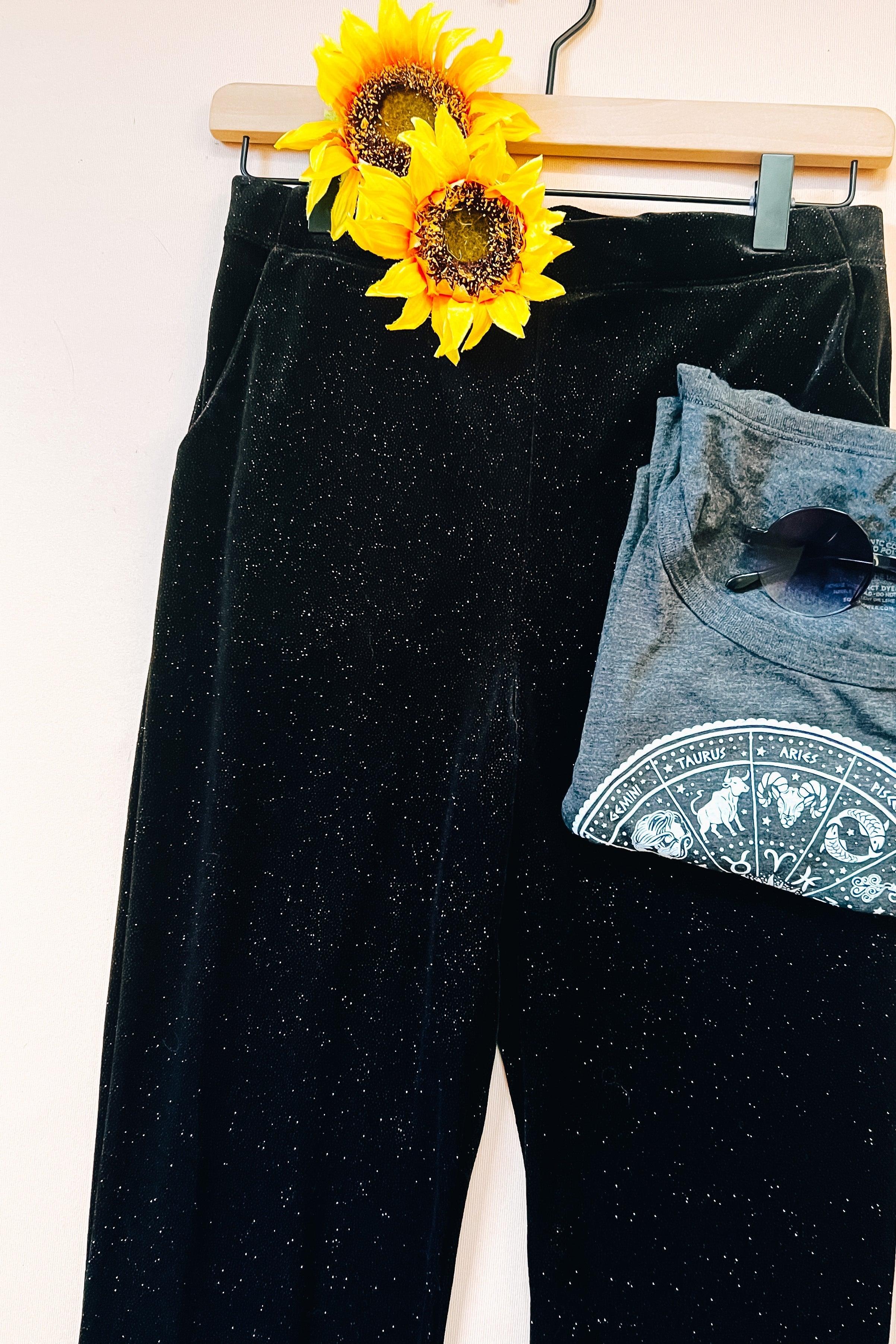 Black glitter velvet bell bottoms paired with folded gray zodiac graphic t-shirt and sunglasses on hanger