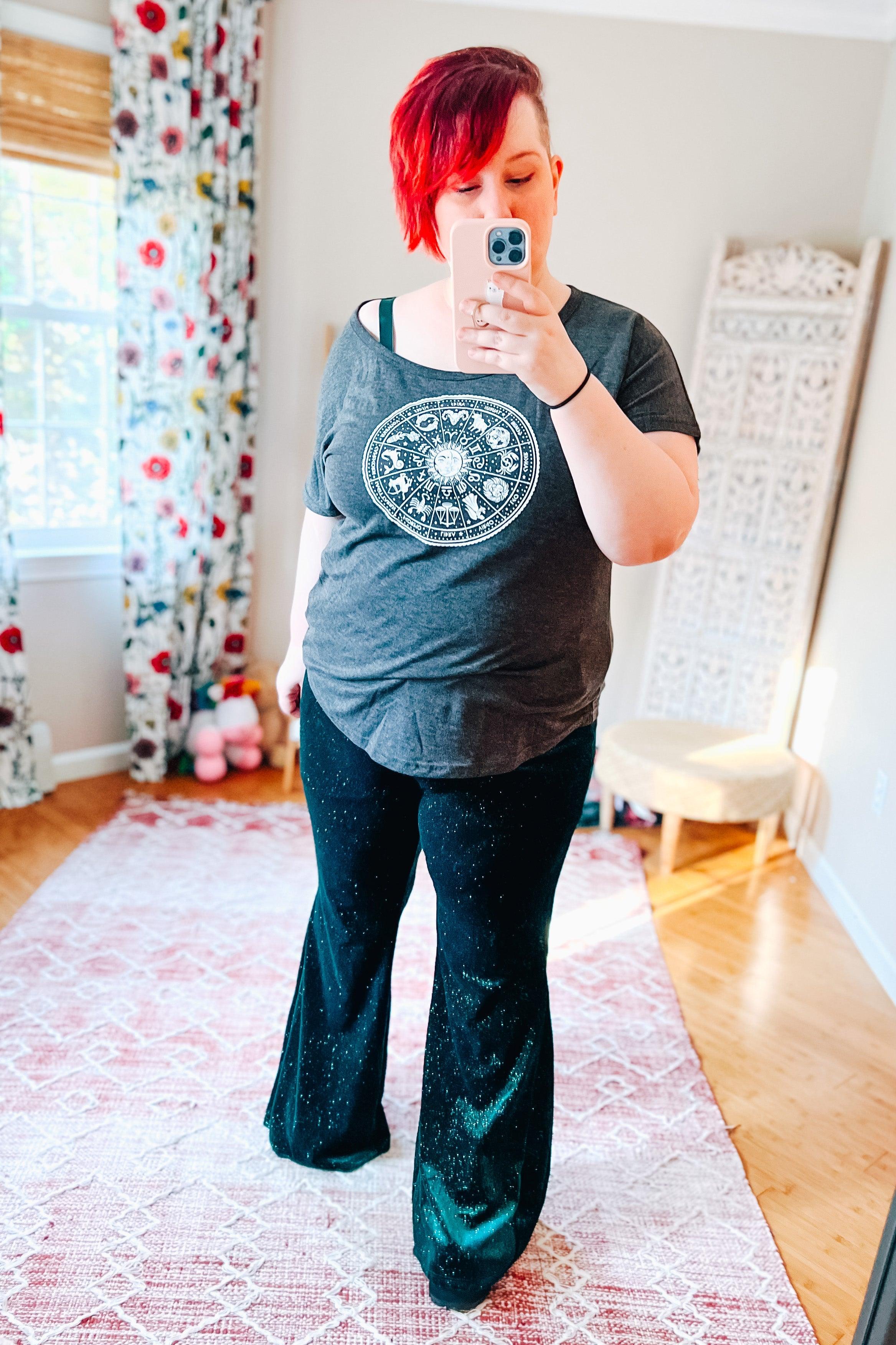 Woman taking selfie wearing black glitter bell bottoms with a dark grey zodiac graphic tee in bright room