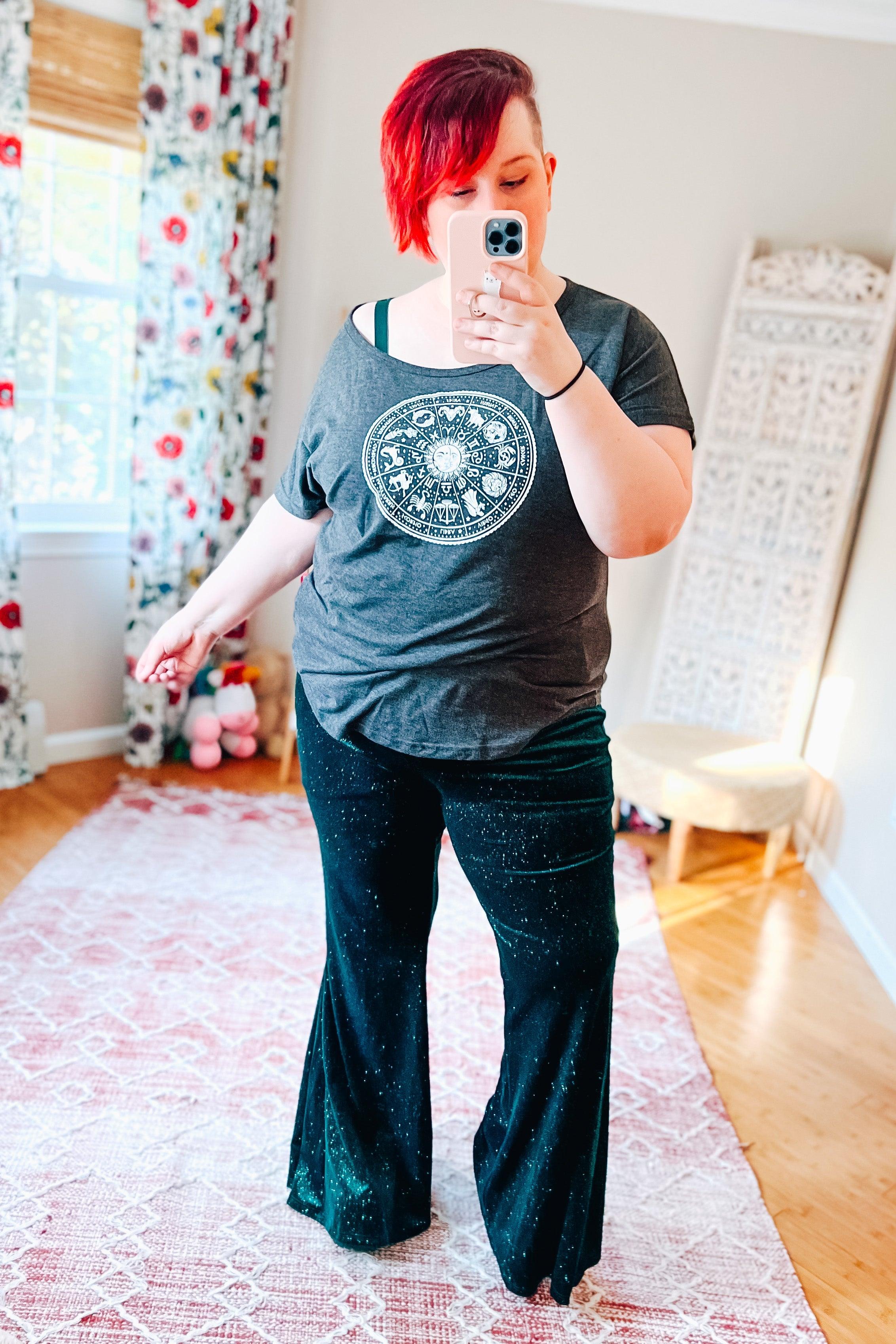 Woman taking selfie wearing black glitter flared bell bottoms and dark grey zodiac graphic t-shirt indoors