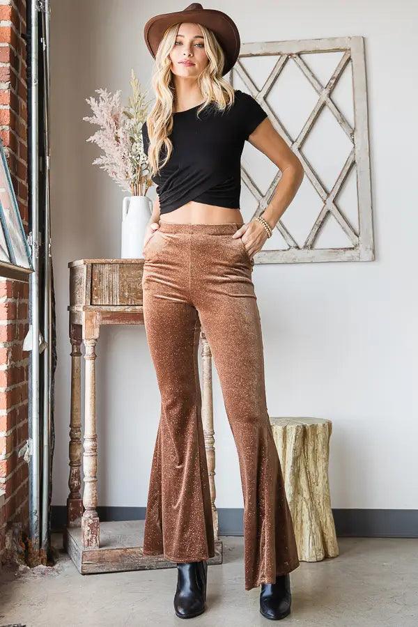 Woman posing indoors wearing gold glitter velvet bell bottoms with black crop top, brown hat, and black boots