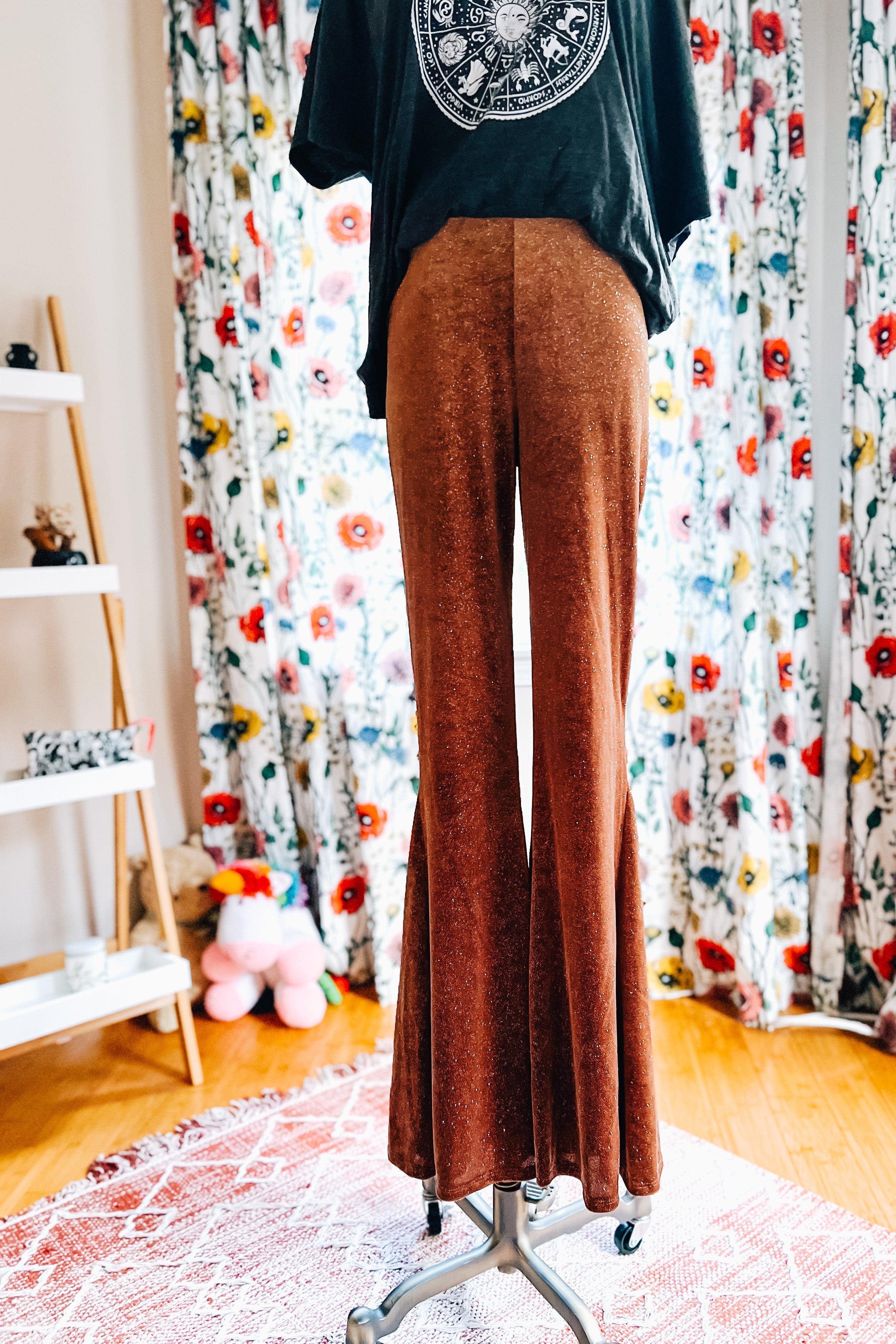 Rust-colored glitter bell bottoms displayed on mannequin with black graphic top against floral curtain background