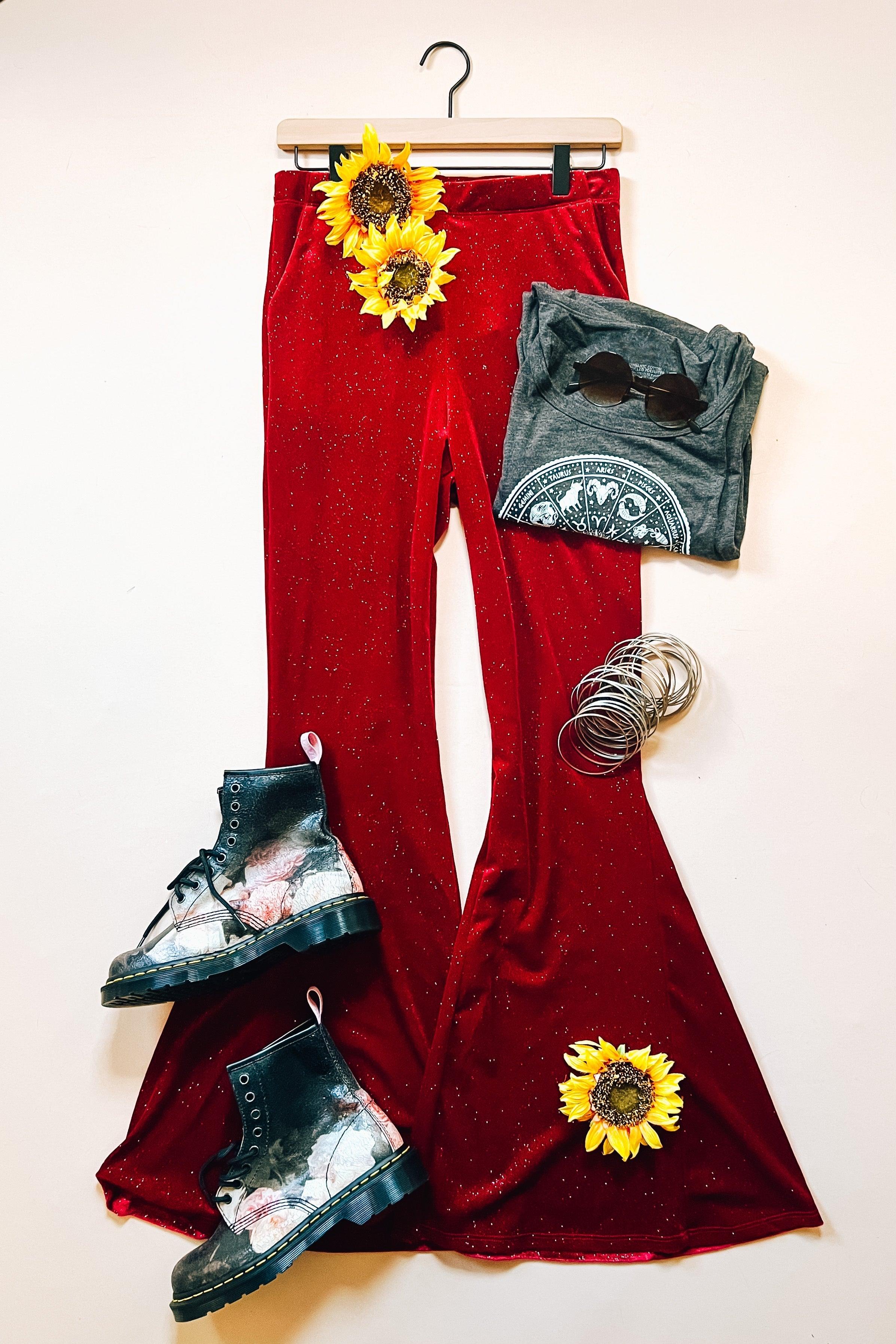 Ruby red glitter bell bottoms styled with distressed black boots, gray graphic tee, bracelets, and sunflowers on white background