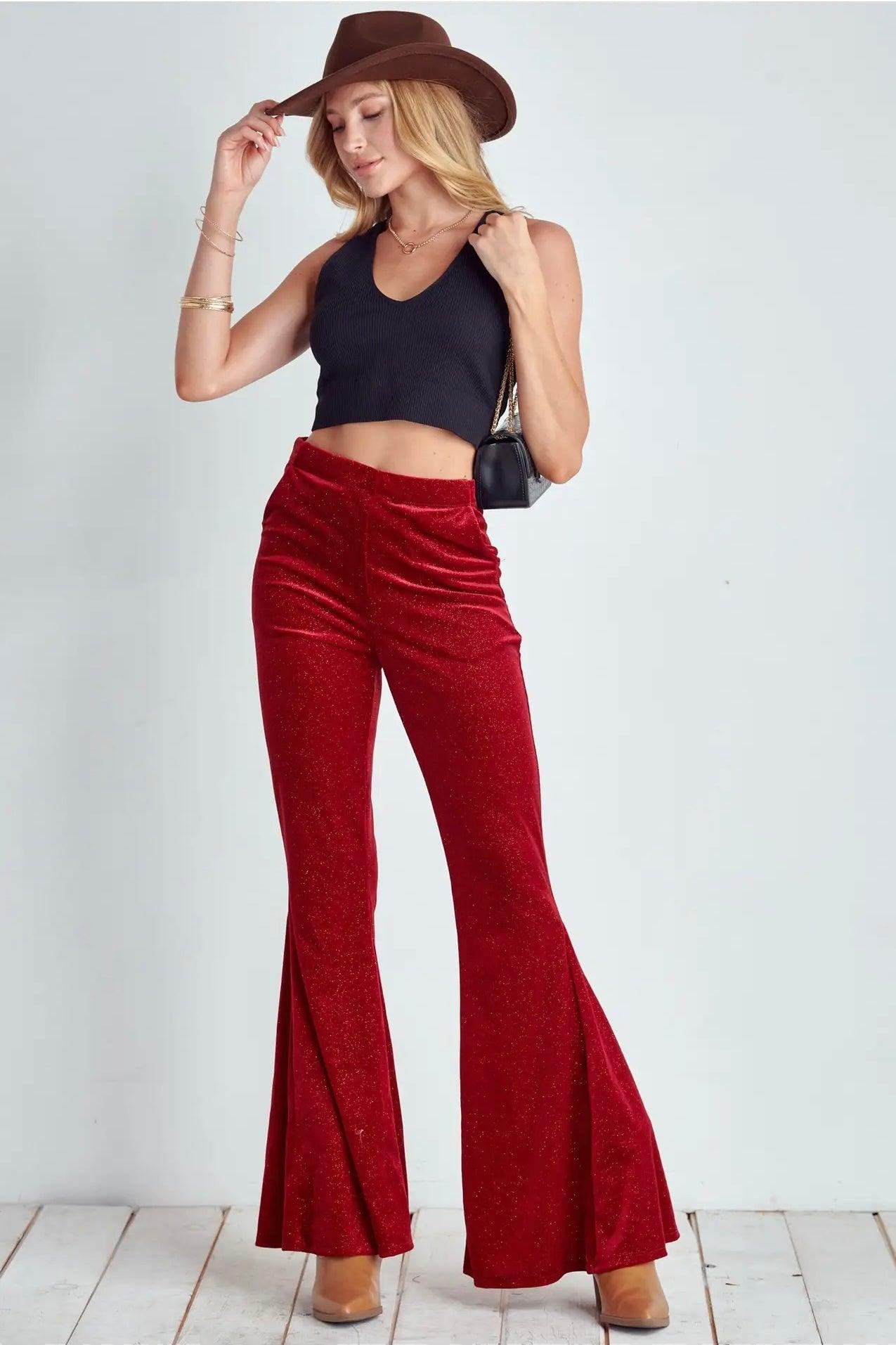 Woman wearing ruby red glitter flare bell bottoms with black crop top and brown hat on white background