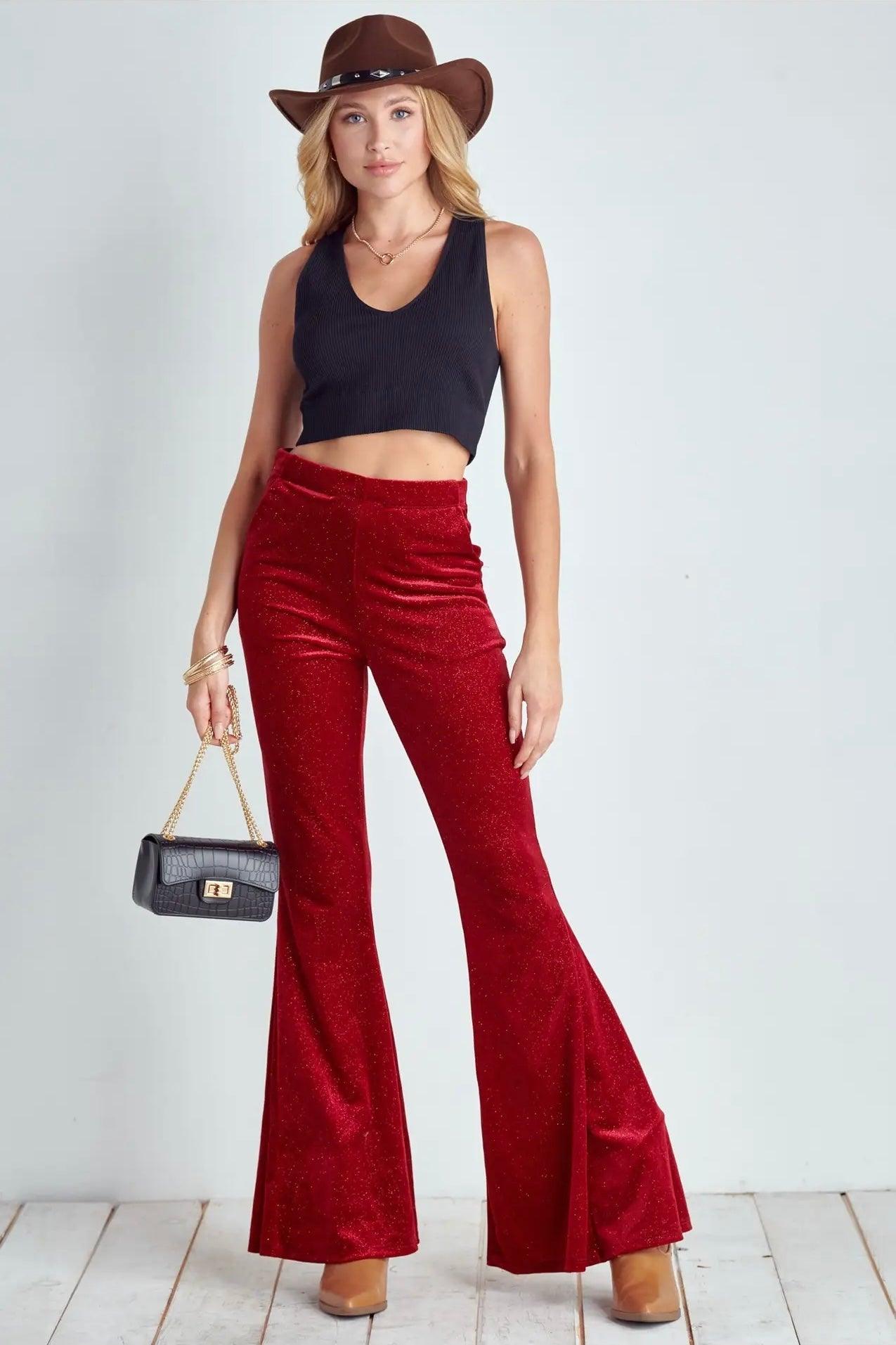 Model wearing ruby red glitter bell bottoms paired with black cropped tank top and brown hat on white background