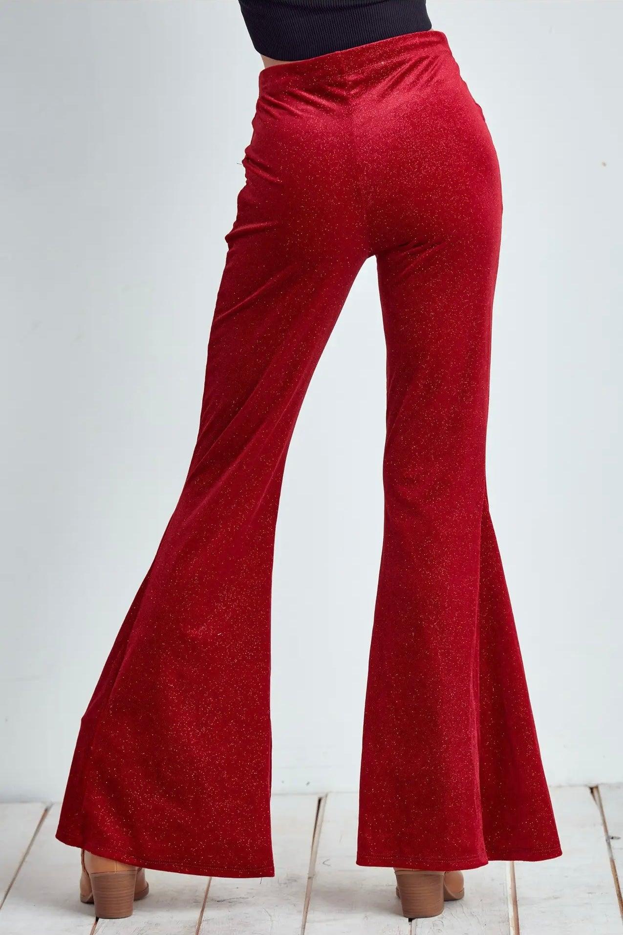 Back view of red glitter velvet bell bottoms worn with black top on white wooden floor background