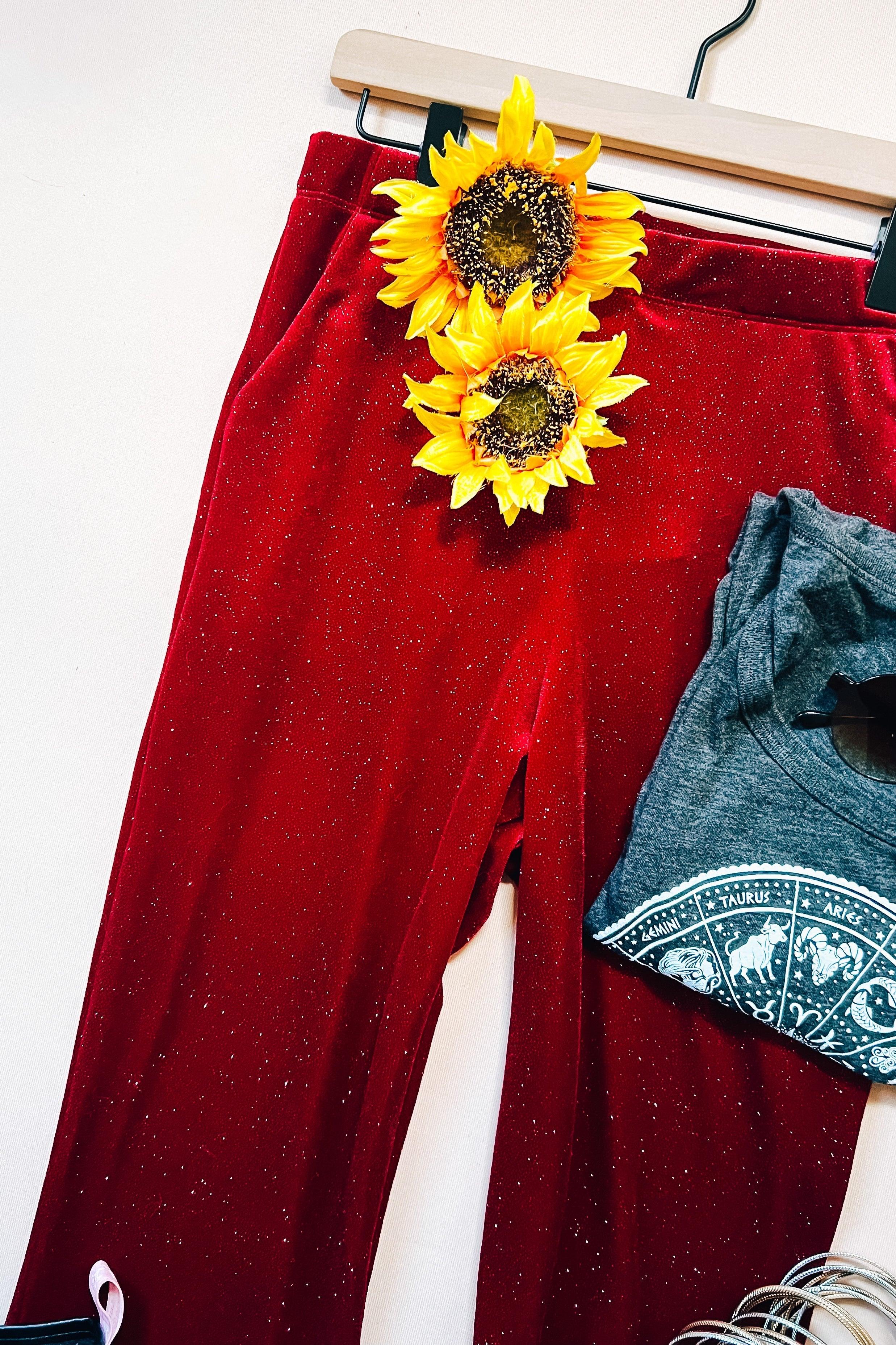 Ruby red glitter bell bottoms displayed with yellow sunflowers and gray zodiac graphic t-shirt on hanger