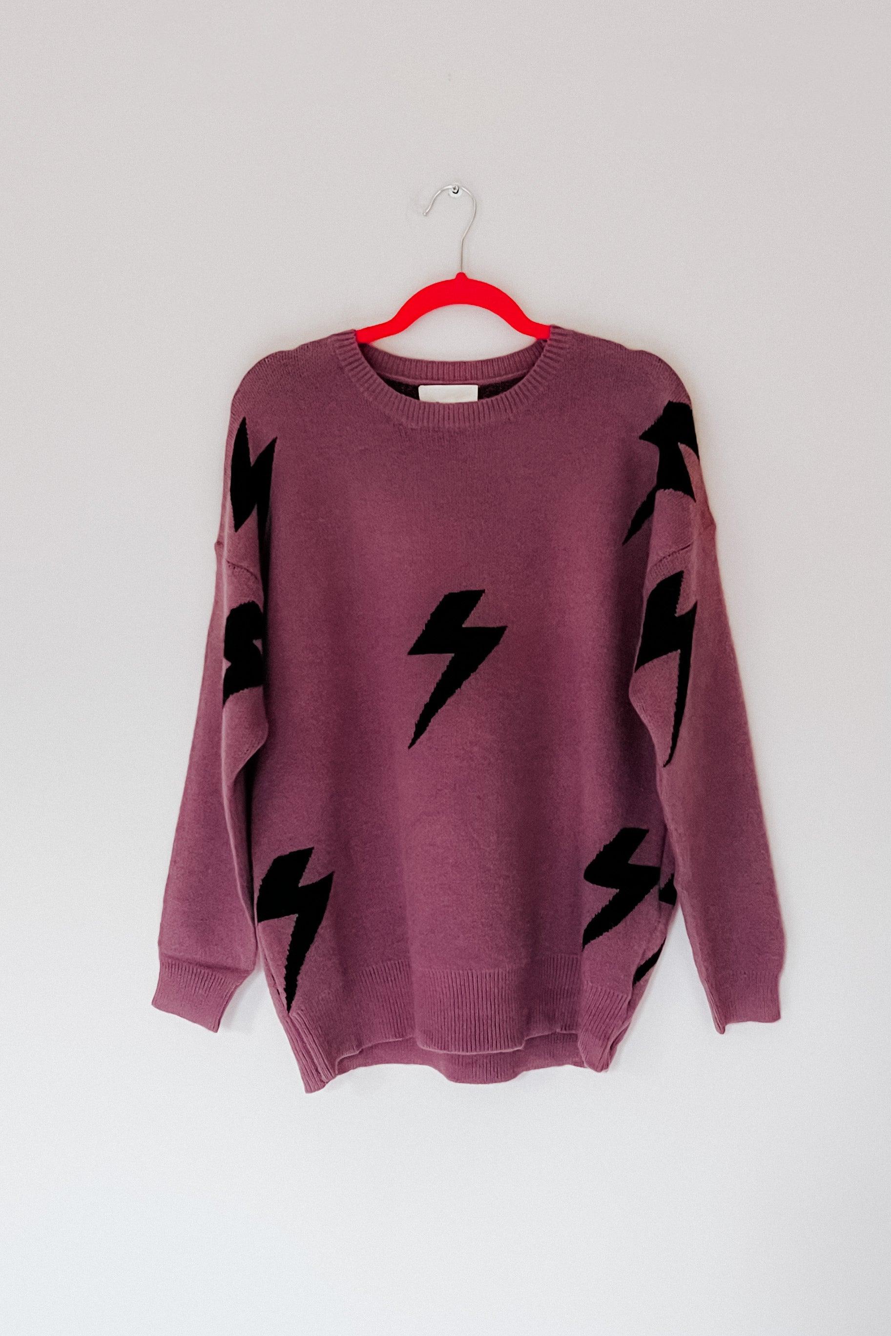 A purple sweater with black lightning bolts hanging from a hanger on a white background