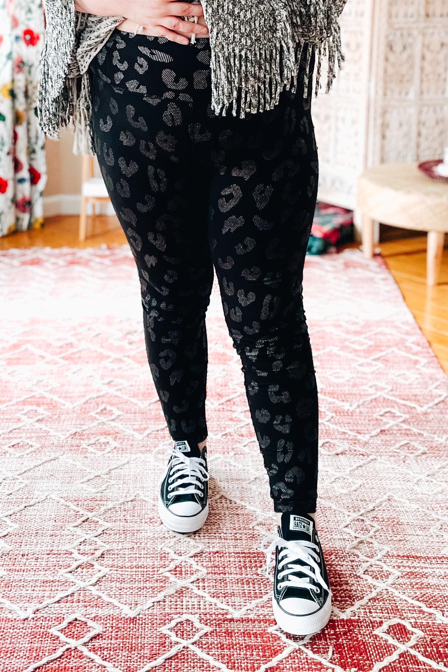Front view of woman wearing black leopard foil print leggings paired with black and white sneakers indoors on patterned rug