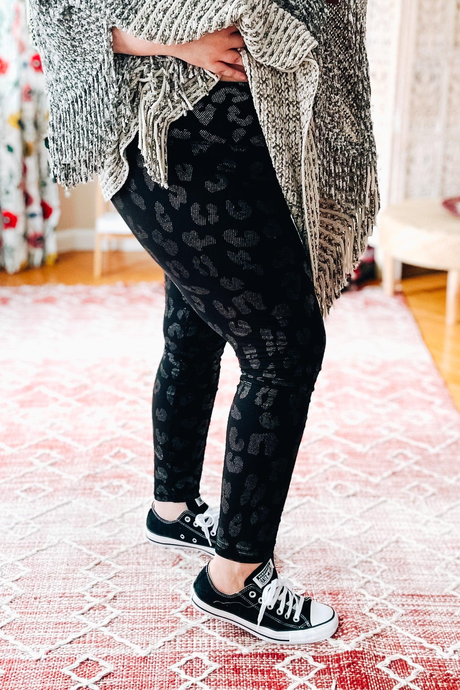Side view of woman wearing black leggings with subtle leopard foil print and black sneakers indoors on patterned rug