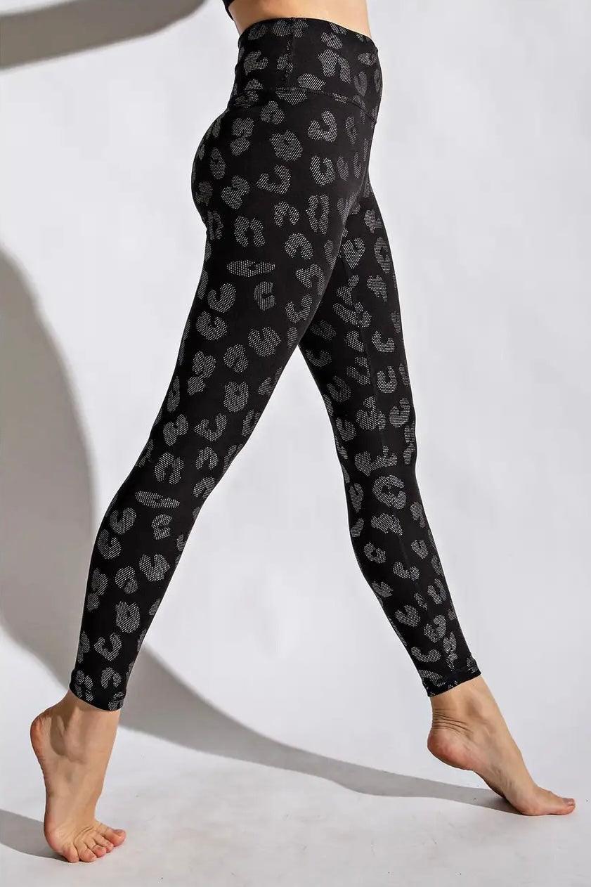 Side view of woman in high-waisted black leggings with subtle dark leopard print standing barefoot on white background