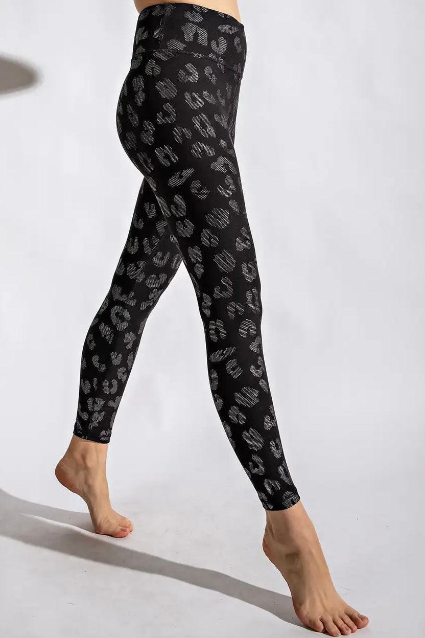Side profile of woman wearing black high-waisted leggings with subtle grey leopard spots standing barefoot on white background