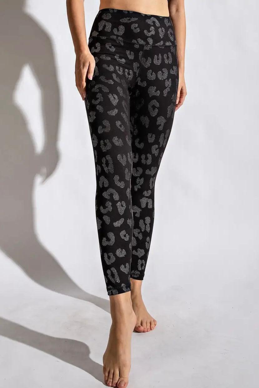 Front view of woman wearing high-waisted black leggings with dark grey leopard spots barefoot on white background