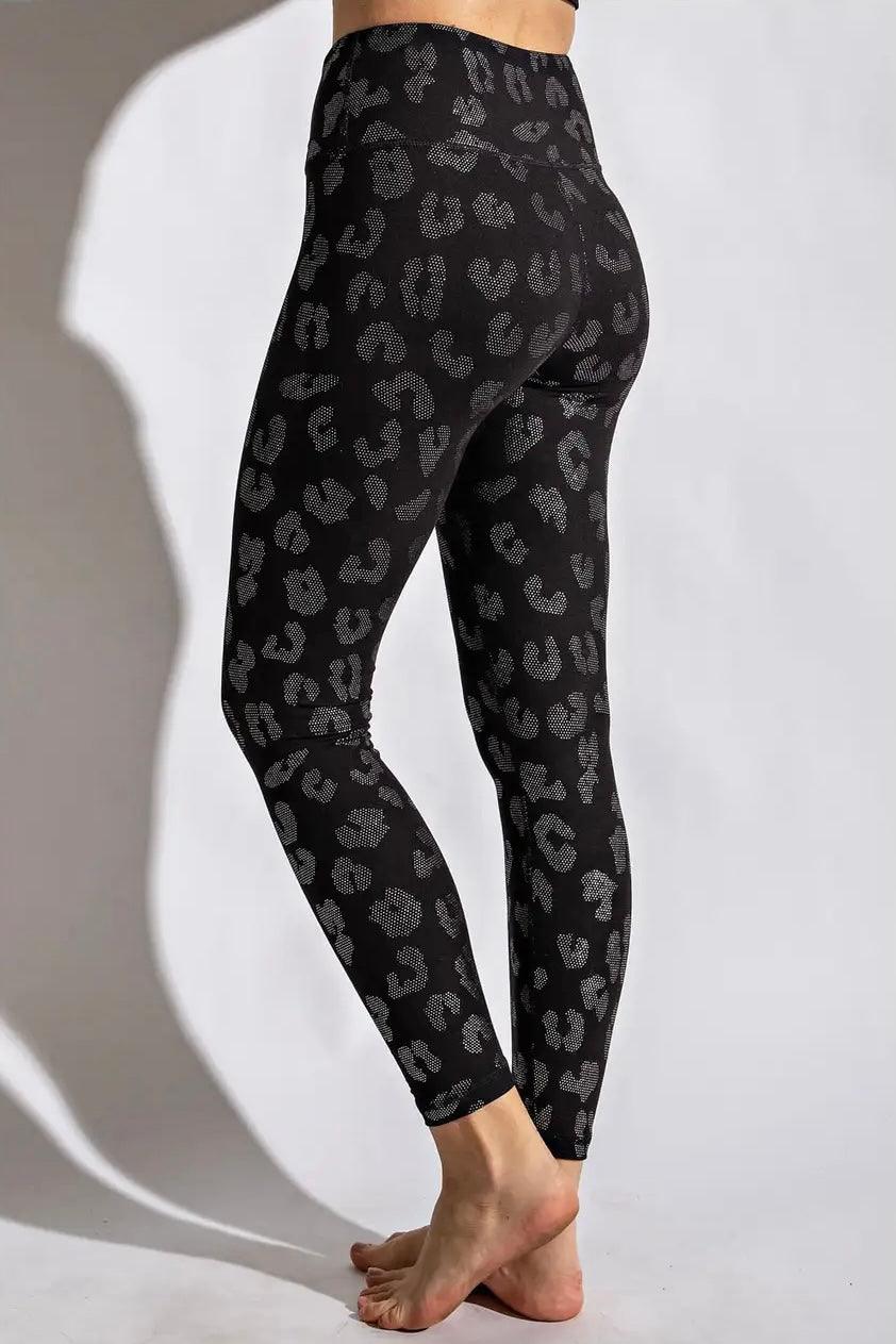 Back view of woman wearing black leggings with dark grey leopard print standing barefoot on light floor