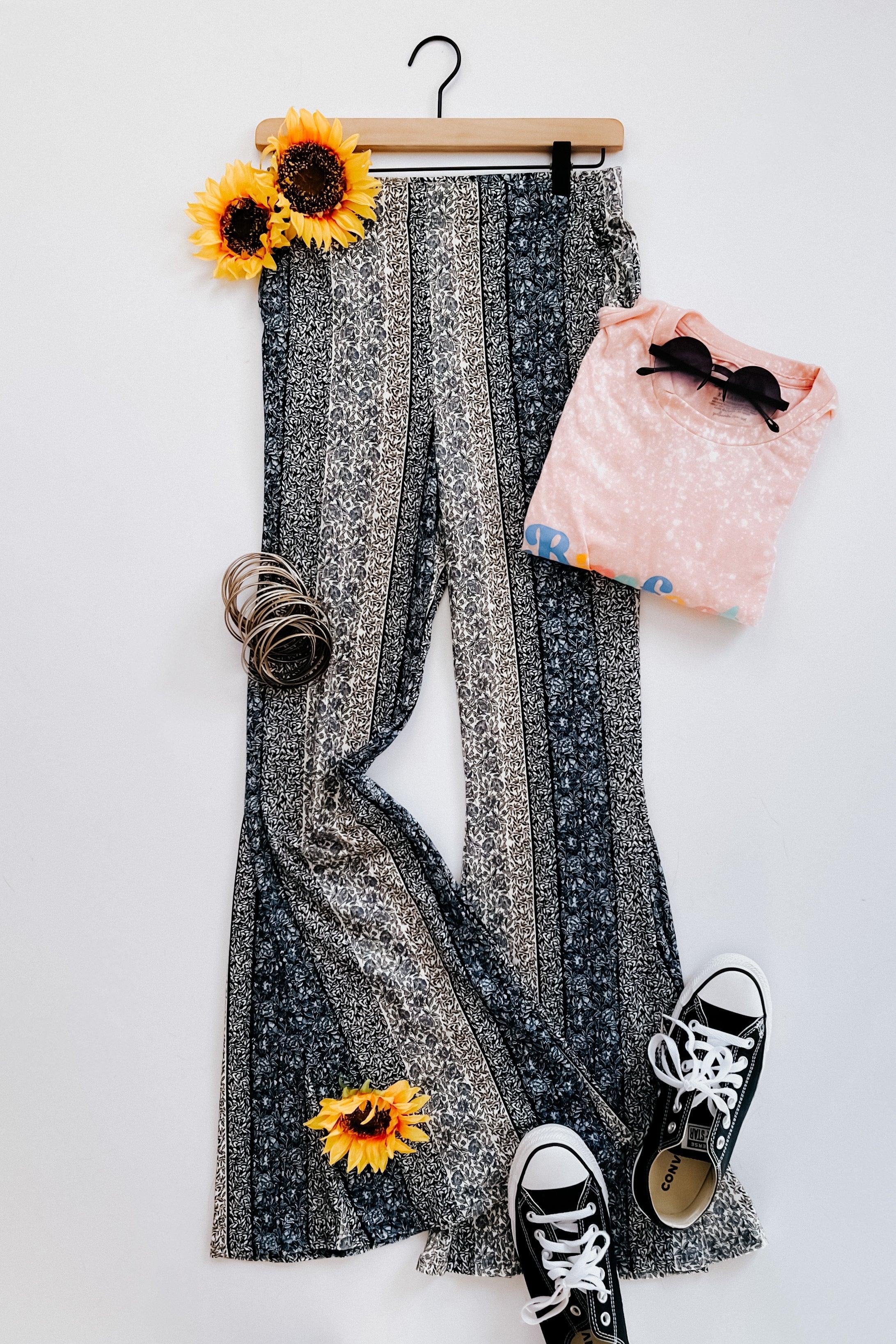 Fleetwood Floral Bell Bottoms in navy with alternating vertical stripe patterns paired with casual sneakers, sunglasses, stacked bracelets, and a soft pink top with sunflowers.